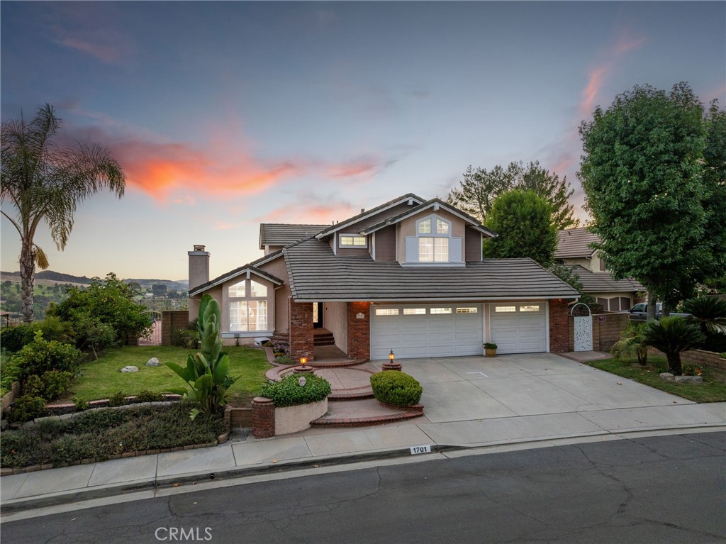Beautifully updated home with panoramic views in the prestigious Regency Hill gated community of Via Verde. Set on an elevated view lot, this residence welcomes you with manicured landscaping, brick planters, and a covered front porch framed by dramatic double iron-and-glass entry doors. Inside, the foyer showcases marble flooring and soaring ceilings that open to the formal living room with a marble fireplace, a large picture window, and an adjacent dining room with iron chandelier and backyard views. The oversized kitchen boasts custom wood cabinetry, granite countertops, stainless steel appliances, recessed lighting, and a breakfast nook overlooking the scenic backyard. Open to the family room, the space offers tiled flooring, a second marble fireplace, and a full wall of sliding glass doors framing the panoramic vistas. A granite-appointed guest half bath and a spacious laundry room with abundant cabinetry complete the main level. Also on the first floor is a secondary primary suite with double doors, tiled floors, sliding glass doors to the side yard, a walk-in closet, and a private ¾ bath with walk-in shower. Upstairs, the luxurious primary suite retreat features vaulted ceilings, double entry doors, and a private balcony with sweeping 180º views. The remodeled spa-inspired bath includes dual sinks, a freestanding tub beneath a chandelier, a glass-enclosed walk-in shower, and a custom walk-in closet. Two additional bedrooms with ceiling fans share a full hall bath. The finished three-car garage offers epoxy floors, storage, and a bench with sink. Outdoors, the entertainer’s backyard showcases panoramic views, year-round sunsets and city lights, a spa, elevated brick gas fire pit, sail shade, and a covered patio spanning the width of the home. The side yards provide a variety of fruit trees and garden space.