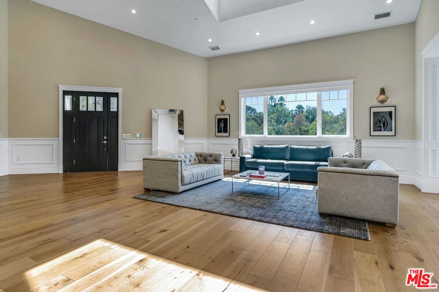 Elegant East Coast inspired gated residence in Tarzana, built in 2014, situated on an expansive 18,000+ sq ft lot. This designer-perfect home showcases quality craftsmanship throughout, featuring brushed white oak flooring, recessed lighting, Restoration Hardware wall sconces, and custom details. Offering 5 bedrooms (one currently used as an executive office/library) and 4.5 baths, the residence blends comfort with sophistication. The open chef's kitchen is designed for both daily living and entertaining, with quartz countertops, a large granite-topped island, top-of-the-line stainless steel appliances including a 6-burner range with pasta faucet, and a butler's pantry. Adjacent to the kitchen is an oversized formal dining room and a spacious living room highlighted by a dramatic two-story ceiling. The main level also includes a guest bedroom suite. Upstairs, a versatile sitting area offers hillside views, along with a convenient laundry room with sink. Two additional en-suite bedrooms complement the elegant primary suite, which boasts dual walk-in closets and a spa-inspired bath with a freestanding Midocean soaking tub, walk-in shower, dual vanities, and makeup counter. The large family room seamlessly connects to a resort-style backyard with a remote-controlled saltwater pool and spa, built-in BBQ island, fire pit, and expansive patio ideal for outdoor entertaining. Additional highlights include a two-car garage with space for a third vehicle, custom window coverings, dual-zoned HVAC, energy-efficient double-panned windows, LED lighting, and a security system with cameras. Conveniently located near The Village, Ventura Boulevard dining and shopping, Warner Center, local parks, and freeway access.