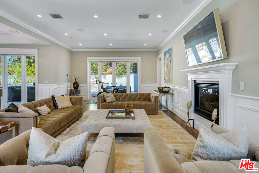 Elegant East Coast inspired gated residence in Tarzana, built in 2014, situated on an expansive 18,000+ sq ft lot. This designer-perfect home showcases quality craftsmanship throughout, featuring brushed white oak flooring, recessed lighting, Restoration Hardware wall sconces, and custom details. Offering 5 bedrooms (one currently used as an executive office/library) and 4.5 baths, the residence blends comfort with sophistication. The open chef's kitchen is designed for both daily living and entertaining, with quartz countertops, a large granite-topped island, top-of-the-line stainless steel appliances including a 6-burner range with pasta faucet, and a butler's pantry. Adjacent to the kitchen is an oversized formal dining room and a spacious living room highlighted by a dramatic two-story ceiling. The main level also includes a guest bedroom suite. Upstairs, a versatile sitting area offers hillside views, along with a convenient laundry room with sink. Two additional en-suite bedrooms complement the elegant primary suite, which boasts dual walk-in closets and a spa-inspired bath with a freestanding Midocean soaking tub, walk-in shower, dual vanities, and makeup counter. The large family room seamlessly connects to a resort-style backyard with a remote-controlled saltwater pool and spa, built-in BBQ island, fire pit, and expansive patio ideal for outdoor entertaining. Additional highlights include a two-car garage with space for a third vehicle, custom window coverings, dual-zoned HVAC, energy-efficient double-panned windows, LED lighting, and a security system with cameras. Conveniently located near The Village, Ventura Boulevard dining and shopping, Warner Center, local parks, and freeway access.