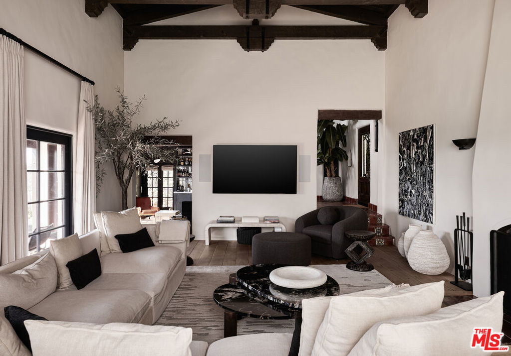 Behind wooden gates in the Hollywood Hills, a reimagined 1920s Spanish residence unfolds with remarkable privacy, architectural integrity, and a city panorama that stretches endlessly beyond its walls. Thoughtfully remodeled by designer Hilary Madigan, the home honors its original character while introducing a level of finish and technology rarely found in historic properties. At the heart of the main level, a dramatic living room is framed by a double-height vaulted ceiling and exposed beams, anchored by a wood-burning fireplace. Arched plaster openings and original tile underfoot guide the natural flow into a formal dining room where French doors open to uninterrupted city views, offering a moment that feels both expansive and intimate.The kitchen is a study in quiet luxury, centered around a La Cornue range and Waterworks fixtures, with integrated Meile appliances and warm, reclaimed wood flooring grounding the space. Throughout the home, the lighting and AV systems have been fully upgraded, with a complete Savant integration for home automation, audio, and visual controlspaired with Lutron Homeworks lighting and a nine-camera security system via Verkada, delivering seamless control and peace of mind. Every bathroom has been redesigned with intention and restraint, outfitted with Waterworks fittings and Toto toilets, continuing the home's throughline of elevated functionality.A sweeping staircase leads to the home's lower level where all three bedrooms are thoughtfully placed. The primary suite, with dual Juliet balconies, includes a custom walk-in closet and dressing area that opens into a tranquil, spa-inspired bath. Two additional bedrooms each offer en-suite baths and bespoke storage. The former basement has been converted into a refined flex spaceideal for a gym, home office, or studio. Designed for effortless indoor-outdoor living, the property invites connection to the surrounding landscape from both levels, while modern systems such as a new HVAC, tankless boiler, and EV-charging-equipped garage ensure contemporary comfort throughout. Offered optionally furnished, and reflecting over $2 million in renovations, this is a home that captures the essence of Old Hollywood while delivering a lifestyle firmly rooted in the present.
