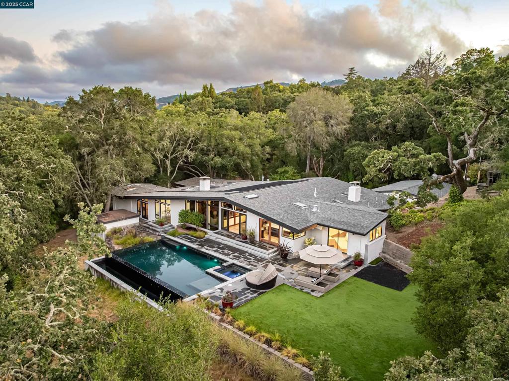 A rare architectural masterpiece by Henry Hill, a founder of the Second Bay Tradition. Privately sited on one of Orinda’s most coveted streets, this landmark estate blends timeless modernist design with nature. Invisible from the road, the home is nestled among majestic oaks and reached by a gated private drive. Enter the home under a sloping beamed ceiling. The formal dining room seats 8-10, beneath skylights. Adjacent is the living room warmed by a grand fireplace. The open-concept interior is characteristic of the architectural style, as the kitchen (under skylights) leads gently down brick steps to the family room. The kitchen is impeccably appointed, with elite appliances, exquisite marble counters, and a matching island over 80 sq ft. Oversized windows draw in cheery morning sun, over the infinity swimming pool, spa, deck, and play area. A spacious office and library/den are found down a brick hallway. Four bedrooms and 3½ bathrooms lie further down. The roughly 350 sq ft principal bedroom is particularly distinctive. A fifth bedroom – perfect as a guest room/in-law suite – is situated at the other end of the home. Parking is easy in the 3-car garage and parking court. This home is an exceptional retreat – minutes to town, yet secluded – just as its architect intended.