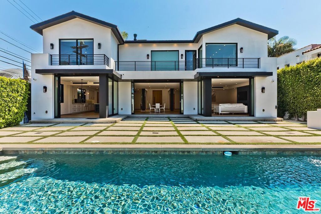 Built in 2017, this modern smart home in Beverly Grove blends sophisticated design with an open floor plan that defines contemporary California living. A dramatic 20-foot skylit entry floods the space with natural light, introducing sleek finishes, soaring ceilings, and wide-plank hardwood floors that flow throughout. The great room concept connects all the main living areas - private front office with patio, spacious family room with fireplace, inviting living room, open gourmet kitchen, and sunlit breakfast area - creating an effortless sense of space. The chef's kitchen is a true showpiece, featuring a large center island with bar seating, Sub-Zero side-by-side refrigerator/freezer, professional Wolf six-burner range with griddle, dual ovens, microwave drawer, and Bosch dishwasher. A wall of floor-to-ceiling glass pocket doors opens to a private backyard oasis with sparkling pool, grassy play area, and built-in grill - perfect for large-scale entertaining, intimate gatherings, or quiet evenings at home. Upstairs, the grand primary suite offers a fireplace, balcony overlooking the yard, custom walk-in closet, and spa-inspired bath with floating vanity, multi-head shower, and freestanding tub. Three additional en-suite bedrooms and an upstairs laundry room provide comfort and convenience.