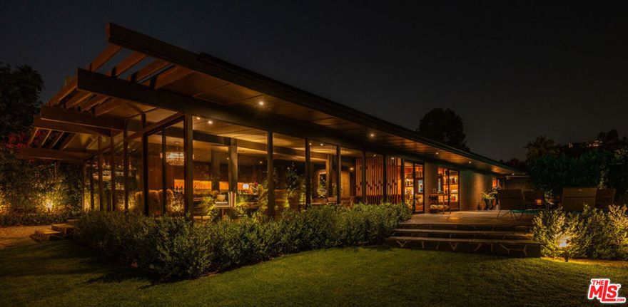 Poised within a sanctuary of architectural beauty and raw natural landscape, this mid-century masterpiece has been reborn--an expression of quiet power, precision, and timeless seduction. Every line refined. Every material intentional. Floor-to-ceiling glass dissolves boundaries between interior and exterior, framing the city skyline like a living work of art. Light moves through the space like liquid, illuminating sculpted forms and impeccable craftsmanship. A complete reinvention from the ground up by Studio Veren: new roof, all new windows, slate floors, Miele appliances, and custom walnut cabinetry throughout. The exterior, once cinderblock, is now fully wrapped in brick--an elegant armor that speaks to permanence and design discipline. Outdoors, flagstone terraces unfold into a private, landscaped retreat. A custom dining banquette captures 360-degree views; a setting that feels cinematic at sunset. Inside, custom furnishings are handcrafted for each room, draped in fabrics from Dedar, Schumacher, Perennials, and Pierre Frey. Vintage lighting and curated accessories punctuate the modern calm with soul and sophistication.