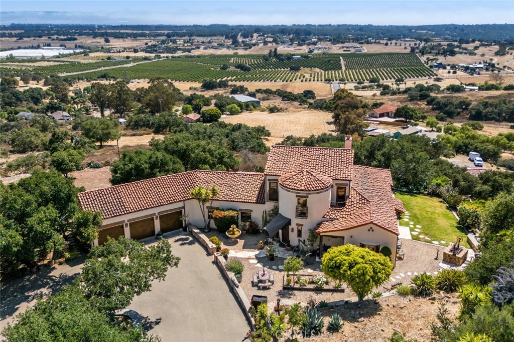 Beyond a private gated entrance, this extraordinary estate unfolds across 10.19 acres studded with avocado trees in the coveted Nipomo East region. Evoking the soul of California's rancho heritage, the property blends Spanish revival architecture with equestrian elegance, offering an exceptional retreat defined by craftsmanship and timeless design. As you pass a classic barn and pastures with welded oil pipe fencing, the estate reveals itself through a graceful circular drive—leading to an attached three-car garage and additional space thoughtfully designed for RV accommodation. A flagstone and brick walkway leads you to an impressive 8 foot mesquite and copper front door and custom copper canopy, setting the tone for the residence within. Spanish tile floors, soaring beamed ceilings, and meticulous copper and ironwork welcome you into a space where artistry meets serenity. The main living area, anchored by a statement fireplace, invites intimate gatherings or quiet moments of reflection. Adjacent, the kitchen balances vintage charm and modern function, featuring bar seating, a generous island, full pantry, wine cellar with antique doors, and a striking vintage Elmira stove and oven—a true homage to tradition. Flowing seamlessly from the dining room, the backyard unfolds into a lush landscape with a signature Santa Maria-style BBQ and native plantings, designed for both celebration and repose. A sunroom offers a refined escape for year-round entertaining, with a fireplace for crisp mornings and double doors opening to breathtaking panoramas stretching to the distant Pacific. The primary suite on the main level exudes tranquility, complete with its own hearth, private sitting area, two walk-in closets, soaking tub, dual vanities, and walk-in shower—every element curated with care and artistry. Upstairs, a cozy landing leads to two additional bedrooms, a shared bath with dual access, and a private balcony where sunsets spill over the valley and ocean beyond. A rare offering where architectural integrity meets expansive natural beauty, this estate is more than a residence—it is a refined way of life.