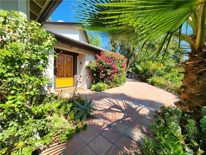 Tucked away in the exclusive, guard-gated community of Hidden Hills, this endearing estate rests on nearly 1.5 private acres and offers a rare blend of rustic charm with modern comforts, at an exceptional value.  Surrounded by lush landscaping, the property feels like a retreat, yet remains moments from the community’s coveted amenities.
The main residence features five bedrooms and three-and-a-half baths.  Light-filled interiors showcase beamed ceilings, wide plank wood floors, and a warm, inviting flow for relaxed everyday living or effortless entertaining. A spacious living room opens to a formal dining room with a fireplace and an updated cheerful kitchen with a sunny breakfast area, while nearly every room extends gracefully to the outdoors for seamless indoor/outdoor living. The private upstairs primary suite offers a cozy fireplace and a balcony to enjoy the evening breezes. Adding to the appeal are the equestrian facilities including a covered corral, a pasture with shelter and a tack room. The grounds include a shaded patio, a hot tub and a generous lawn area.
Residents of Hidden Hills enjoy access to 25 miles of bridle trails, three riding arenas, a community clubhouse with pool, tennis & pickleball courts, and a performing arts theater, all within the award-winning Las Virgenes School District.