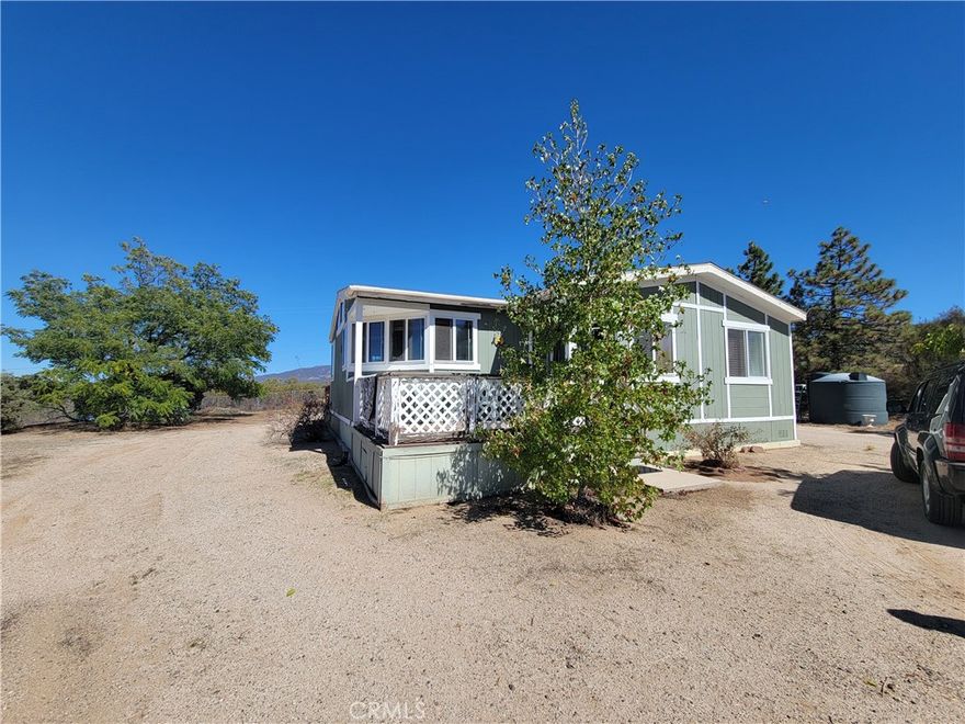 Enjoy peace, privacy, and panoramic views from this inviting 3-bedroom, 2-bath home nestled on a usable 5-acre parcel. Thoughtfully designed for comfort and functionality, this home features front and rear decks, perfect for relaxing or entertaining. Inside, the living and dining areas include a cozy pellet stove—ideal for chilly winter nights. The spacious kitchen has a center island, built-in office area, and a pantry. A wall of windows fills the space with natural light and showcases sweeping views of the surrounding landscape. French doors open onto the rear patio, extending your living space outdoors. You'll find ample storage throughout the home, including large closets . Flooring includes tile in bathrooms, laminate in the main living spaces, kitchen, main bedroom and carpeting in the other 2 bedrooms.  For those who love to work on projects or need extra storage, a separate workshop with three rooms provides endless possibilities. There's also a tall timber-framed structure with a roof and open sides—formerly used for RV storage—with potential for many future uses.  The fully usable property is fully fenced and has mature pine trees, offering plenty of space for horses, farm animals, gardens, orchards, or whatever your vision may be.