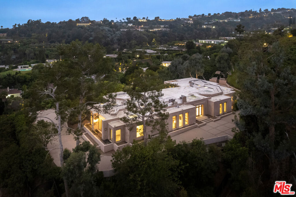 Completely Renovated & Move-In Ready. Perched atop an ultra-private knoll in the prestigious Trousdale Estates, this recently built and fully remodeled residence is secured by stately contemporary gates and commands panoramic views stretching from city lights to the Pacific Ocean. Blending practical simplicity with striking elegance, the home offers both refinement and comfort at every turn. A sweeping 300+ ft driveway leads to dramatic grounds and a residence designed for modern living. The grand formal foyer opens to a 75-ft art gallery hallway with soaring 12-ft ceilings, skylights, and custom sandstone floors an architectural showcase bathed in natural light, ideal for displaying a world-class art collection. The oversized living room is wrapped in floor-to-ceiling glass walls that frame breathtaking vistas. Designed for seamless entertaining, this space connects effortlessly to the new saltwater pool and expansive outdoor living areas. The gourmet, eat-in kitchen is a chef's dream, centered around a striking fireplace and appointed with top-tier appliances, a generous butler's pantry, and bespoke finishes. The adjacent family room continues the home's theme of glass-wrapped spaces and panoramic outlooks. The primary suite is a private retreat, complete with a refreshment station, fireplace, dual spa-inspired bathrooms, expansive walk-in closets, and an adjoining study. Three additional bedroom suites ensure comfort and privacy, complemented by a large laundry and utility room as well as an elegant arrival lounge . For future flexibility, the property offers the option to expand onto the additional lot - or preserve it as a natural extension for enhanced privacy and security.
