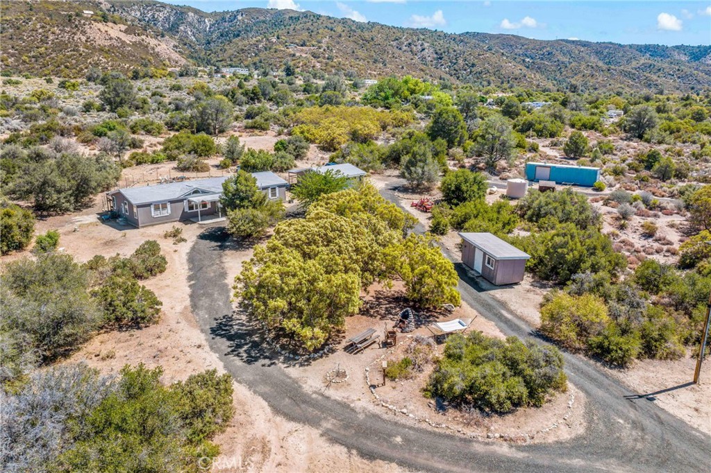 Spacious Country Living with Modern Comforts on 5 Usable Acres. Discover the perfect blend of space, rural charm and modern technological touches with this 4-bedroom, 2-bathroom, 1,782 sq ft single-story manufactured home on a permanent foundation. Set on 5 flat, fully usable acres with RV hookups, mature landscaping, this property offers endless opportunities—enjoy walking or riding trails, a small shooting range setup, peaceful camping spots, evening stargazing, or romantic solar lit walks. The black gravel circular driveway allows easy vehicle access and helps control water erosion and leads to a detached 2-car garage, wood storage shed, and large metal storage container for ample storage. The newer garage is insulated w workshop layout & EV/welding ready 220V service. The fenced backyard is perfect for pets, featuring a separate dog kennel area or “catio” for your feline friends. Inside, fresh interior paint and durable vinyl flooring create a move-in ready appeal w fiber optic internet, smart appliances and Ring security. The open floor plan boasts a large kitchen with a center island, black appliances and breakfast area flowing seamlessly into the family room, complete with a cozy fireplace, built-in desk, and ceiling fan. A versatile bonus/exercise room with a closet could serve as a 5th bedroom. Spacious secondary bedrooms each feature a custom color-changing ceiling fan/light fixture with dimmer, and share a well-appointed hall bath with a tub/shower combo. The primary suite offers vaulted ceilings, abundant natural light, a walk-in closet, and a private bathroom with separate tub and shower plus tiled flooring. Located on a gentle rise overlooking the valley, this home offers evening city-light views and is just a short walk from local schools. Too many upgrades to list...check out the complete inventory of repairs and renovations on the 'supplement' page. Whether you’re seeking space for hobbies, animals, or simply room to breathe, this property delivers.