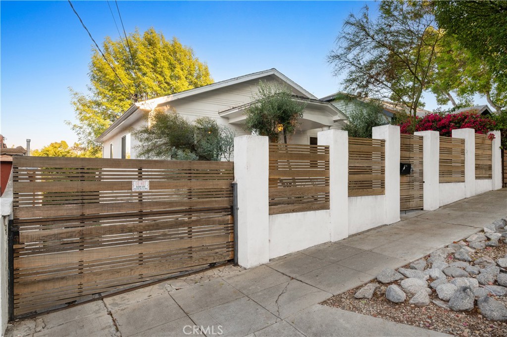 Tucked behind a privacy fence, this updated home offers a thoughtfully designed blend of indoor-outdoor living at the nexus between Silver Lake and Echo Park. A one-of-one custom carved wooden front door opens into an airy floor plan featuring light-toned wood flooring throughout the living, dining, and flexible-use spaces. The kitchen showcases a clean navy and white palette, accented with brass hardware, a premium Wolf range, and direct access to a spacious balcony —well-suited for outdoor dining or casual gatherings.
The primary suite includes a generously sized bedroom, a pass-through closet, and an attached bathroom with dual sinks, a walk-in shower, and marble countertops. A guest bathroom and a dedicated laundry area complete this level.
Downstairs, two additional bedrooms offer tall ceilings and ample storage. A covered patio leads to a private backyard with hardscaped and open areas designed for entertaining, recreation, or quiet relaxation —providing a flexible space that can be tailored to a variety of outdoor uses.
The home has also been outfitted with solar panels. A gated driveway provides parking for multiple vehicles. Located near local dining, shopping, and neighborhood amenities, this residence offers a well-rounded living experience in a sought-after location.