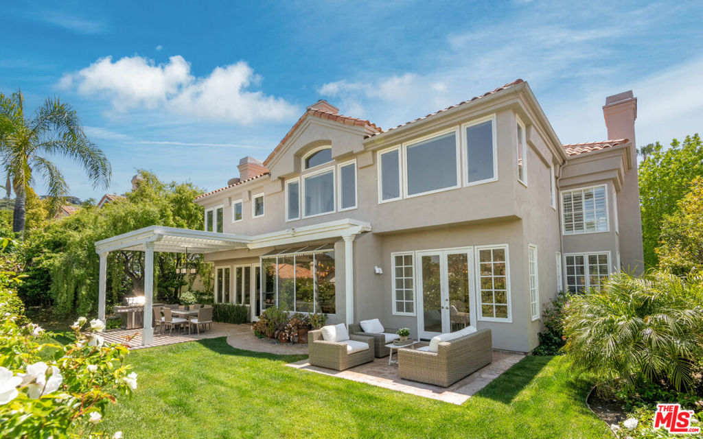 This beautifully redesigned five-bedroom, five-bath residence offers a grand sense of scale paired with refined design and modern comforts. With over 4,000 square feet of thoughtfully planned living space including both formal and casual gathering areas, this home was made for elegant entertaining and relaxed everyday living. The spacious, private backyard follows the theme outdoors with lush landscaping, a trellis-covered dining area, and generous space to unwind, host, or enjoy time with family and friends. This home delivers style, space, and serenity in equal measure. Located in the highly desirable "Carrara" enclave by J.M. Peters, celebrated for its thoughtful architecture and airy, light-filled floor plans, the home is positioned to take full advantage of mountain ridge views. Thoughtfully remodeled, the layout is gracious and welcoming, ideal for both entertaining and everyday living. A set of custom wrought iron double doors opens into a dramatic entry with sky-high ceilings, a sweeping staircase, and a central skylight that bathes the interior in natural light. Wide-plank shutters, oversized windows, and French doors create seamless indoor-outdoor flow, while crisp white walls, chiseled-edge stone floors, and rich dark hardwood flooring add texture and warmth throughout. Ambient lighting, designer fixtures, and three upgraded fireplaces lend an elevated, curated feel. The formal living and dining areas flow effortlessly into a mirrored bar alcove with Calacatta Vadara quartz counters and a built-in wine fridge, perfect for entertaining. At the heart of the home, the open-concept kitchen and family room serve as the ultimate gathering space. The bright gourmet kitchen features waterfall-edge Calacatta Vadara quartz counters, a large center island, white cabinetry with pull-out drawers, and a full suite of stainless steel appliances. A double-wide pantry offers generous storage, and the adjoining family room opens through French doors to a shaded outdoor dining area, accented with an iron chandelier and surrounded by a lush grassy yard lined with white climbing roses. Upstairs, the grand primary suite is a peaceful retreat, accessed through double doors and framed by vaulted ceilings and panoramic views. Hardwood flooring continues throughout, and the suite includes a cozy sitting room with a fireplace, Hunter Douglas designer blinds, and an additional wardrobe wall for extra storage. The en-suite bath is spa-inspired, featuring dual vanities, a frameless glass shower with mosaic tile floors, a freestanding soaking tub, stone flooring, and an expansive walk-in closet designed for both function and luxury. Additional highlights include a full-size laundry room with built-in storage and a three-car garage with a Tesla charger. As a resident of Calabasas Hills, you'll enjoy access to two beautifully maintained community pools, a private park, and close proximity to the award-winning Bay Laurel Elementary School. The home is ideally situated near the scenic trails of Calabasas Park, upscale shopping and dining at The Commons, the popular Saturday farmers market in Old Town, and top-rated schools. This is Calabasas living at its most refinedwarm, modern, and move-in ready.