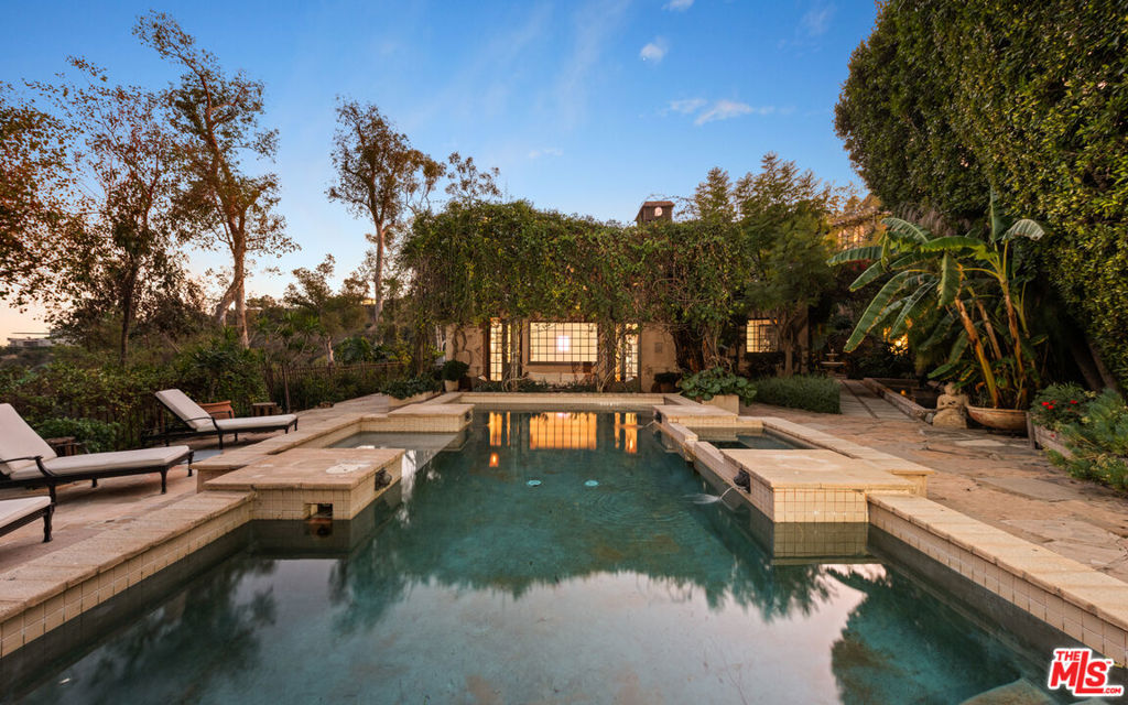 Perched in Beverly Hills, this enchanting Mediterranean retreat combines timeless design with lush natural surroundings. Exposed wooden beams, arched doorways, and hand-laid brick floors create a warm, rustic elegance throughout. Sunlit interiors feature spacious living areas, a chef's kitchen with high-end appliances, and a serene primary suite with a spa-like bath. Step outside to discover a private oasis with a sparkling pool, serene courtyards, and vine-covered pergolas. Stone pathways wind through landscaped gardens, leading to a rooftop patio with breathtaking panoramic views. Additional highlights include a detached guest suite, custom office, and the charm of a bell tower-inspired room. A perfect blend of privacy and proximity to Sunset Boulevard, this property offers an unparalleled lifestyle in one of LA's most coveted locations.