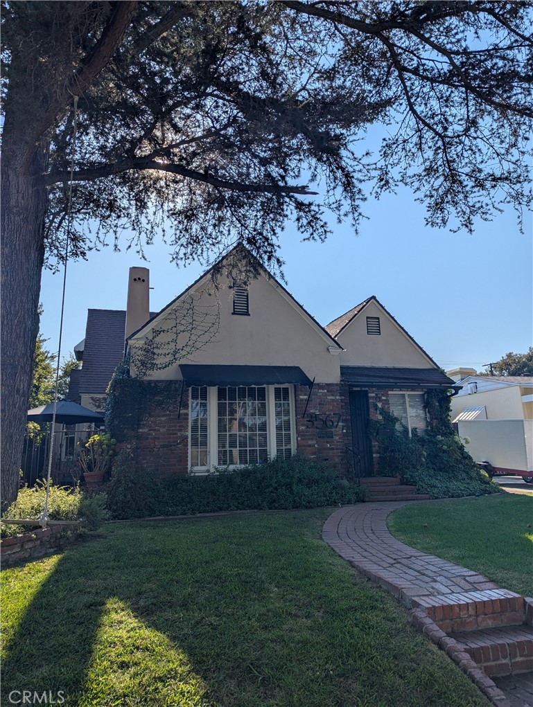 Step into this timeless 1926 Tudor Revival, blending architectural detail with tasteful modern updates. Just a short walk to charming local shops and restaurants. The dramatic living room features high coved ceilings, vintage pressed-tin ceiling panels, and original mahogany trim. The adjacent formal dining room includes a character-rich bay window and warm wood accents. A separate office/study/library with vaulted ceiling includes a built-in mahogany bookcase, drop-down desk, and spacious drawers. The entry door is original mahogany with an inlaid beveled oval glass window—a true one-of-a-kind. The updated kitchen boasts granite countertops, ebony cabinetry with pull-out drawers, and modern appliances, leading to a cozy breakfast nook and adjacent laundry room. Downstairs offers 2 bedrooms and a remodeled full bath. The highlight is a spacious rear family room with beamed ceilings, a brick gas fireplace with heat-exchanger insert, rustic wood mantel, and French doors opening to a private backyard with two covered patios. Upstairs features two generously sized bedrooms with vaulted ceilings, walk-in closets, and a remodeled full bath (2023). Additional features include: Two covered rear patios, ideal for entertaining, block wall for added privacy, detached 3-car garage or 2-car + finished hobby room with upstairs loft (studio or storage). Lovingly maintained and thoughtfully updated, this rare gem offers vintage elegance, flexible space, and a prime location in one of Long Beach’s most beloved historic neighborhoods.