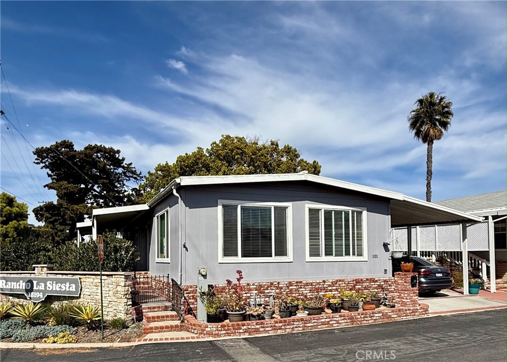 This is a well-maintained manufactured home with a charming exterior featuring a combination of gray siding and red brick accents. The home has a classic gable roof and large, white-framed windows that allow plenty of natural light inside.
The front of the home has a landscaped brick planter adding a cozy and inviting touch. The property includes a covered carport with white lattice panels, offering shaded parking.
There is a private and relaxing space with artificial grass for easy maintenance. It includes a covered patio area for outdoor seating, relaxation and entertaining, with a lush mix of greenery and privacy fencing.
This house is perfect for someone looking for a comfortable and stylish manufactured home in a well-kept community.