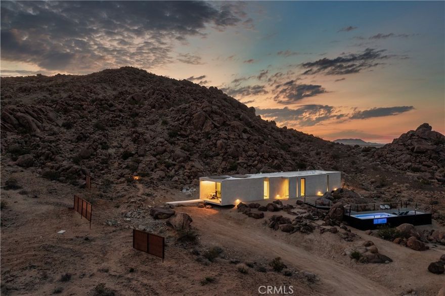 A rare architectural statement built directly into Joshua Tree’s iconic boulders, The Prism House lives like a private nature reserve — a seamless extension of the boulders themselves. Set on 5 acres that back up to protected, boulder-strewn land, it lives like 100+, offering complete privacy and an otherworldly connection to the landscape, all just 10 minutes from town. Designed by URBARC Architects and developed by KUD Development, this one-of-a-kind retreat was completed in 2022 using the cutting-edge RSG3D concrete and foam system — delivering unmatched strength, insulation, and energy efficiency. Every inch reflects design intention and craftsmanship: JennAir appliances, Eso Surfaces custom terrazzo tile, Fleetwood sliders, riftsawn oak cabinetry and doors, electric window blinds, custom LED lighting, and a built-in library with a reading nook that frames the desert light. The layout features dual primary suites plus a powder room, balancing flexibility for both personal use and high-end short-term rental income. Already a six-figure income generator, the home comes fully equipped with its branding, professional photography and video, Instagram presence, and an established luxury rental operation — making it a true turnkey opportunity. Recognized on a global stage, The Prism House earned the Platinum Winner in Household Architecture at the International Architecture & Design Awards 2025 (IADA) and the People’s Choice Award 2024 from the LOOP Design Awards. Qualifying for Airbnb Luxe (one of only a few in the desert) further elevates its prestige and earning potential. A rare work of architecture designed to disappear into the desert — and yet, impossible to forget.