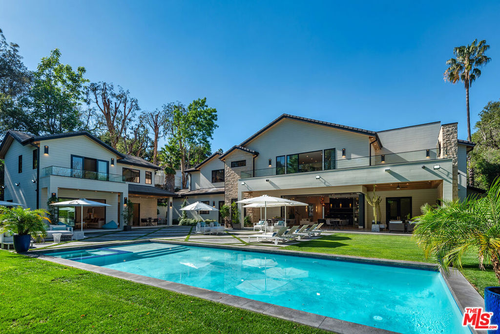 Next-level luxury within the exclusive Royal Oaks enclave of Encino. Situated at the quiet end of a cul-de-sac just off famed Woodvale Road, this private estate caters to the most discerning homeowner with an endless litany of luxurious amenities. Beyond the oversized gates, towering hedges and array of security cameras, the property features dual two-car garages and a custom pivot entry door that reveals an elegant black and white color palette warmed by wide-plank white oak floors, a striking rose gold chandelier, a glass-enclosed wine cellar, and a captivating view of the exceptional outdoor entertaining space. Artfully designed and meticulously crafted, this light-filled California contemporary home features an open, modern floor plan and a true chef's kitchen with two islands. The formal entry flows into the living room and a chic bar area, accented by bespoke black brickwork. Enjoy an immersive experience in the state-of-the-art home theater. There are three main level bedrooms to accommodate family members or staff. This eight-bedroom residence also has an elevator connecting the first and second levels, and includes a stunning second-level primary suite with a fireplace and a fashionista-worthy closet. Disappearing sliding doors open to a second floor private balcony with views of the serene grounds and no other homes or yards. An additional 1100 sf rooftop loft with outdoor kitchen, built-in bench seating, and space for a huge outdoor screening space, which provides a secluded setting for al fresco dining and views of starlit nights. It's the perfect place for the kids to have their own entertaining area within the safe confines of the property. The beautifully landscaped backyard features a sparkling pool, covered bar, outdoor lounge, lots and lots of space for resort-style chaise lounging, a ping pong area, and a great half-court basketball court. The detached two-story guest house offers 1,400 square feet of additional living space, with a gourmet kitchen with barstool seating, living room, laundry, two bedrooms and three bathrooms, a private retreat in itself. It truly is a second home on the property. Lush landscaping and meticulous detail define this exceptional property, offering incomparable design, privacy, and lifestyle in a premier location. It's exclusive, it's elevated, it's bespoke design meets secluded comfort.