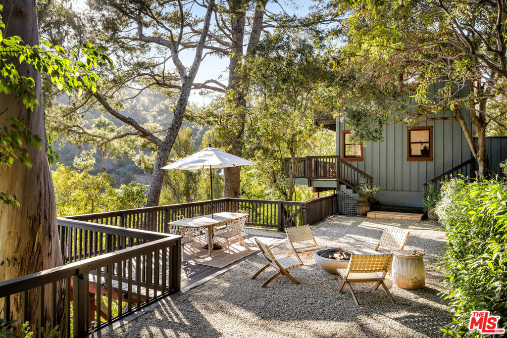 Tucked into the Hollywood Hills, this Mid-Century ranch features a quarter-acre of layered gardens, lush views from every room, and a history of housing a variety of creatives throughout the years. Original character remains lovingly intact, now paired with updates that honor both function and form. Step into a living room with vaulted wood-beam ceilings, a wood-burning fireplace, and timeless details bathed in light from a wall of windows. The space flows into a dining room where French doors open to sun-drenched decks, a flat yard with a fire pit, and a hidden outdoor room perfect for creating or relaxing. The home additionally features five bedrooms, six baths, and a spacious family room ideal for canyon living. The home has been upgraded to include solar panels, an EV charger, and a two-car garage with abundant storage. It is set in the Outpost Estates, a storied neighborhood where artists and professionals live among the oaks, this home is moments from the Hollywood Bowl, Runyon Canyon, Studio City, and beloved cafes and restaurants.