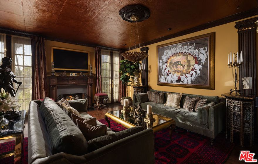 A rare opportunity to acquire a spectacular two-story townhome in West Hollywood's coveted Norma Triangle, meticulously remodeled and designed as a breathtaking homage to Old Hollywood glamour and Gilded Age sophistication. Every element, from the architecture to the art, was chosen for its unrivaled quality and rarity, resulting in a space that is as warm and inviting as it is undeniably exclusive.The design philosophy was simple yet uncompromising: source the absolute best that could be found, with pieces shipped in from around the world. As the homeowner acquired this entire collection specifically for this residence, this is an unprecedented opportunity to acquire a fully furnished, turnkey Gilded Age-style masterpiece. This light-filled two-bedroom, two-and-a-half-bath residence offers exceptional flow for gracious entertaining. The main level welcomes guests through a dramatic entryway before proceeding to the formal living room, anchored by a museum-quality Grand Tour white marble bust of Apollo and a spectacular fireplace serving as the room's focal point. Stunning copper leaf tin ceilings crown the living room, dining room, and breakfast room, adding warmth and period-appropriate grandeur throughout the entertaining spaces. The adjacent dining room showcases custom furnishings sourced from around the globe, with double doors opening onto a covered terrace: a unique outdoor retreat finished with faux grass flooring and faux boxwood walls creating a private, immersive environment.A charming alcove breakfast room features bold and elegant design, with a dramatic gold leaf chandelier fashioned in a delicate leaf pattern suspended above. The well-appointed kitchen provides direct access to both the breakfast nook and the dining room, featuring a Viking six-burner gas range, dishwasher, and refrigerator/freezer. A dedicated laundry room houses a Samsung washer and dryer.The powder room is a showpiece unto itself, featuring black crocodile-embossed vinyl walls, heavy tin faux brick wainscoting, a tin ceiling with crown molding, and nineteenth-century Flemish infinity mirrors. Descending the staircase, one arrives at the lower level, which is situated on the second floor of the building, offering a second private entrance directly from the internal hallway for convenient access to the bedroom level of this gorgeous townhome. Immediately upon arrival, a tucked-away home office nook provides an ideal work-from-home space, featuring a Country French antique walnut desk with pull-out extension. An adjacent closet beneath the stairs offers discreet storage for electronic equipment and hookups. The sophisticated guest suite features a spacious bedroom with its own ensuite bath, providing comfortable privacy for overnight visitors. The primary suite is a true retreat, accessed through double doors that open into a small vestibule. To one side, a modern butler's pantry has been created, featuring a black lacquer storage cabinet with gold feet, a hidden refrigerator/freezer, and a black quartz countertop breakfast bar. The generous walk-in closet is also accessed from this vestibule. The bedroom itself features fabulous brocade damask draperies and a luxurious primary bath with separate tub and shower and dual vanities. Sliding doors open onto a private terrace with faux boxwood walls and recently installed electric awnings, providing a serene outdoor escape. Additional features include two dedicated parking spaces within the secure garage and a private storage room. The building offers a south-facing swimming pool, fitness center, and rooftop deck with phenomenal views, all behind secure entry.Ideally situated near Sunset Plaza, SoHo House, Santa Monica Boulevard, and moments from Rodeo Drive. Available vacant or delivered as a fully furnished, turnkey masterpiece.