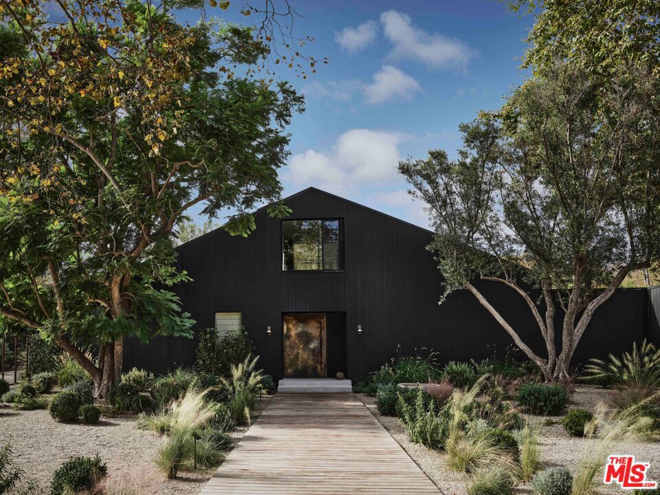 Tucked within the serene Bonsall Canyon - a coveted Malibu enclave renowned for its tree-lined streets and peaceful seclusion just minutes from Point Dume and Zuma Beach - 6153 Bonsall Drive is a Belgian farmhouse-inspired retreat that seamlessly blends contemporary design with Malibu's laid-back luxury. At once bold and tranquil, this 7,050-square-foot estate rests on 1.3 acres of lush, park-like grounds, offering a lifestyle that celebrates both architectural artistry and the surrounding natural beauty. The vision for this home was brought to life by Vanessa Alexander of Alexander Design, who balanced minimalism and warmth in every detail. Arriving at the home is an experience in itself, with a grand yet grounding processional walkway leading to the striking exterior, clad in custom Shou Sugi Ban wood that lends texture and depth to its barn-like silhouette. Inside, natural light floods the open spaces, illuminating finishes such as imported stone, raw brass accents, and hand-applied plaster walls. Every material feels tactile and intentional, creating an atmosphere of understated sophistication. The heart of the home is an expansive kitchen and family room, where 20-foot vaulted ceilings and seamless indoor-outdoor flow establish a perfect balance of grandeur and livability. The space opens to a sprawling outdoor area, complete with a 60-foot pool, an open-air kitchen, and a dining area designed for unforgettable evenings under Malibu's endless skies. This interplay between interiors and exteriors extends throughout the property, inviting a constant connection to the outdoors. The primary suite takes full advantage of its setting with floor-to-ceiling windows that frame lush views. It is a serene retreat, featuring an oversized walk-in closet and a spa-inspired bathroom outfitted with a soaking tub and a glass-walled marble shower. Thoughtfully designed for both function and indulgence. The home's interiors are curated yet approachable. Custom lighting fixtures, including the sculptural pendant by Rogan Gregory and Pick Up Stick chandelier by Cam Crockford, act as striking focal points, while entertainment spaces such as a game room with a custom pool table and a dedicated movie room add an air of casual elegance. The layout is expansive yet intimate, designed for both grand hosting and quiet evening at home. Outside, the property's grounds offer a private escape. A resort-style pool is surrounded by custom daybeds, an orchard, and a flourishing herb garden, creating a sense of retreat that feels both luxurious and organic. The neighborhood offers seamless access to Malibu's most iconic beaches, scenic hiking trails, and acclaimed dining destinations. Widely featured in Architectural Digest, Elle Decor, Vogue, and The New York Times, 6153 Bonsall Drive is a residence that transcends trends. It embodies the enduring spirit of Malibu: a place where natural beauty, refined design, and soulful living converge. This estate is not just a home; it is an experience, one that leaves an indelible impression with every detail.