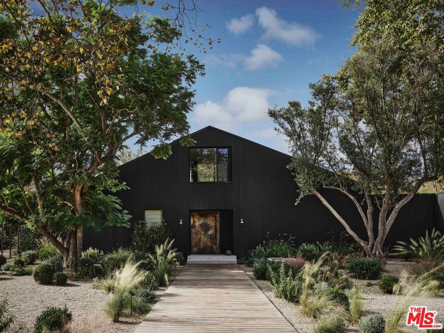 Tucked within the serene Bonsall Canyon - a coveted Malibu enclave renowned for its tree-lined streets and peaceful seclusion just minutes from Point Dume and Zuma Beach - 6153 Bonsall Drive is a Belgian farmhouse-inspired retreat that seamlessly blends contemporary design with Malibu's laid-back luxury. At once bold and tranquil, this 7,050-square-foot estate rests on 1.3 acres of lush, park-like grounds, offering a lifestyle that celebrates both architectural artistry and the surrounding natural beauty.  The vision for this home was brought to life by Vanessa Alexander of Alexander Design, who balanced minimalism and warmth in every detail. Arriving at the home is an experience in itself, with a grand yet grounding processional walkway leading to the striking exterior, clad in custom Shou Sugi Ban wood that lends texture and depth to its barn-like silhouette. Inside, natural light floods the open spaces, illuminating finishes such as imported stone, raw brass accents, and hand-applied plaster walls. Every material feels tactile and intentional, creating an atmosphere of understated sophistication. The heart of the home is an expansive kitchen and family room, where 20-foot vaulted ceilings and seamless indoor-outdoor flow establish a perfect balance of grandeur and livability. The space opens to a sprawling outdoor area, complete with a 60-foot pool, an open-air kitchen, and a dining area designed for unforgettable evenings under Malibu's endless skies. This interplay between interiors and exteriors extends throughout the property, inviting a constant connection to the outdoors.  The primary suite takes full advantage of its setting with floor-to-ceiling windows that frame lush views. It is a serene retreat, featuring an oversized walk-in closet and a spa-inspired bathroom outfitted with a soaking tub and a glass-walled marble shower. Thoughtfully designed for both function and indulgence.  The home's interiors are curated yet approachable. Custom lighting fixtures, including the sculptural pendant by Rogan Gregory and Pick Up Stick chandelier by Cam Crockford, act as striking focal points, while entertainment spaces such as a game room with a custom pool table and a dedicated movie room add an air of casual elegance.  The layout is expansive yet intimate, designed for both grand hosting and quiet evening at home. Outside, the property's grounds offer a private escape. A resort-style pool is surrounded by custom daybeds, an orchard, and a flourishing herb garden, creating a sense of retreat that feels both luxurious and organic. The neighborhood offers seamless access to Malibu's most iconic beaches, scenic hiking trails, and acclaimed dining destinations. Widely featured in Architectural Digest, Elle Decor, Vogue, and The New York Times, 6153 Bonsall Drive is a residence that transcends trends. It embodies the enduring spirit of Malibu: a place where natural beauty, refined design, and soulful living converge. This estate is not just a home; it is an experience, one that leaves an indelible impression with every detail.