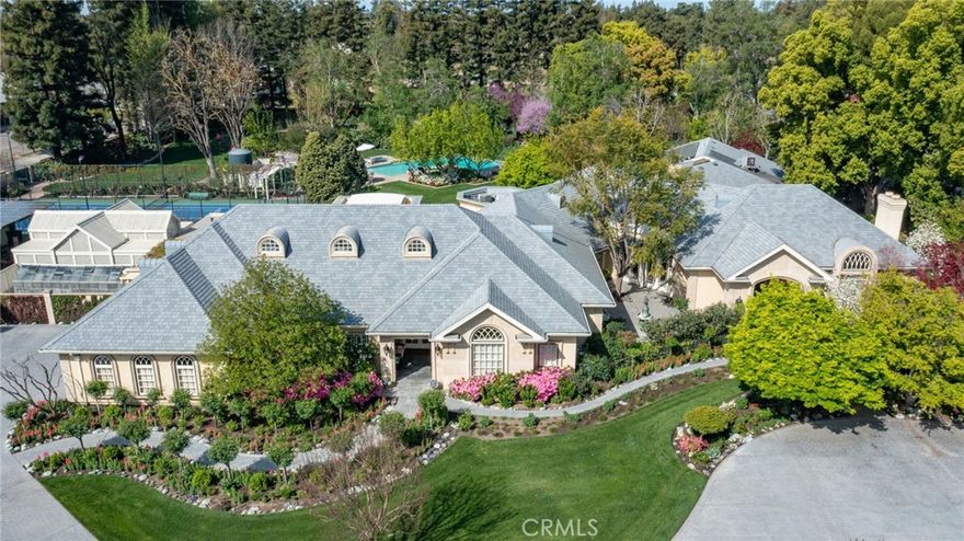 This French Inspired Traditional Home, offering five bedrooms and six and one half bathrooms is situated on a 3 acre parcel in North West Fresno, and is truly a One-of-a-Kind property. It has been transformed over the years to what is today a peaceful and luxurious 9258sf estate, featuring the finest of quality and workmanship. It allows for living and entertaining in an atmosphere surrounded by meticulously maintained lushly landscaped grounds, filled with beautiful roses, various annuals and perennials, mature trees, expansive lawns, koi pond, tennis court, batting cage, greenhouse, vegetable garden, and a sparkling swimming pool. The elegant interior boasts vaulted and coffered ceilings, elegant wood moldings, marble flooring, wood wainscotting, arched wood windows, chandeliers, and too many amenities to mention. The spacious rooms include a grand formal living room, spacious formal dining room, family room, office, a chef's kitchen with center island, informal dining area and walk-in pantry, game room, wet bars, sunroom, and a powder room.The bedroom wing includes an elegant primary suite featuring a fireplace, an abundance of windows, dressing area, and a beautifully appointed en-suite bath. Three additional bedrooms. 2 offer en-suite bathrooms. A den and a hall bath complete this wing. The fifth bedroom with 1/2 bath is isolated and is situated near the game room. Other amenities include a three car garage, slate roof, owned solar and a gardeners maintenance yard.