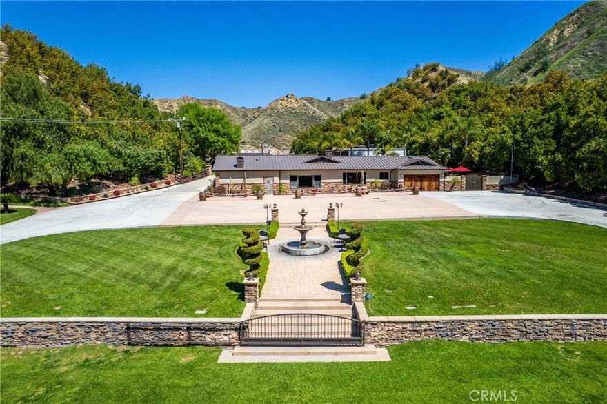 Welcome to a one-of-a-kind luxury ranch estate nestled in the exclusive Live Oak Canyon of Redlands, California. Spanning over 24 private acres across five separate parcels, this extraordinary property offers unmatched privacy, natural beauty, and refined rustic living. Lined with approximately 400 mature avocado trees and supported by two private wells, multiple water storage tanks, and a backup generator, the estate is both self-sustaining and turnkey. At the heart of the property is a custom-designed 3,200+ sq ft ranch-style residence with 3 bedrooms and 3.5 bathrooms, thoughtfully crafted with authentic character and modern comforts. Enter through grand custom doors into a warm, inviting great room with floor-to-ceiling windows that draw in natural light and overlook a beautifully curated desert-modern courtyard, designed with clean lines, native landscaping, and tranquil seating areas that bring a high-end, resort-style ambiance to everyday living. Host with flair at your cowboy cool inspired bar, complete with refrigeration, sinks, and rustic shiplap walls. Enjoy time in the open-concept kitchen flows into a panoramic dining room where glass walls frame the breathtaking backyard oasis, perfect for daily living or unforgettable gatherings. The primary suite is a private sanctuary, featuring a spacious walk-in shower, luxurious steam bath, and direct access to the backyard retreat. Two guest bedrooms are located on the opposite side of the home, connected by a Jack and Jill bathroom, offering separation from the main entertainment areas. Outside, the experience continues with a resort sized pool featuring a swimup bar, oversized spa, grotto, cascading waterfalls, and fire features all operated via smart controls. A fully equipped outdoor BBQ kitchen and a bathroom complete with outdoor steam shower room by the pool offer additional spa-like luxury. Additional structures include an oversized carport, detached rustic garage with salon-style doors, and multiple storage units. This estate is being sold fully furnished, making it the ultimate turnkey ranch retreat.