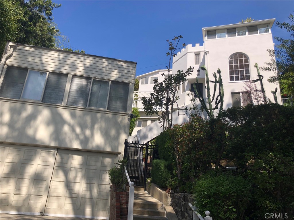 Incredibly located in the Iconic Bronson & Beachwood Canyons of the Hollywood Hills sits a castle like compound with views of the Oaks & downtown LA. At the top of its stairs, enter this 4 bedroom 3 bathroom home & walk into its large living room with hardwood floors & architectural windows.  Just off the living room there is an alcove to a primary bedroom with a private balcony & access to two larger patios & gardens.  A good size kitchen with upside potential has stairs that go down to another primary bedroom which has its own kitchen, balcony, & separate entrance.  Could be a home office or nanny suite.  The laundry and bonus room are also located on this bottom level with access to patios.  Wind your way up the spiral staircase & to the tree top level of the house and there are 3 bedrooms & 1 bathroom.  2 of the bedrooms have enclosed sitting porches.  Please note the Rec Room over the Garage has an additional living space that is complete with private patio & separate entrance located above the large garage. Ideal for workspace.  Patios & gardens throughout as well as perfect for private al fresco dining & indoor/outdoor living.  This retreat is in town and steps away from Bronson Park, shopping, dining, & all major studios.  This compound inspires one's creative juices to just keep flowing. 
--