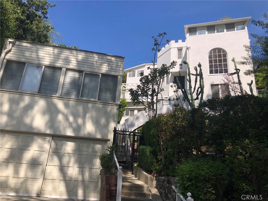 Incredibly located in the Iconic Bronson & Beachwood Canyons of the Hollywood Hills sits a castle like compound with views of the Oaks & downtown LA. At the top of its stairs, enter this 4 bedroom 3 bathroom home & walk into its large living room with hardwood floors & architectural windows.  Just off the living room there is an alcove to a primary bedroom with a private balcony & access to two larger patios & gardens.  A good size kitchen with upside potential has stairs that go down to another primary bedroom which has its own kitchen, balcony, & separate entrance.  Could be a home office or nanny suite.  The laundry and bonus room are also located on this bottom level with access to patios.  Wind your way up the spiral staircase & to the tree top level of the house and there are 3 bedrooms & 1 bathroom.  2 of the bedrooms have enclosed sitting porches.  Please note the Rec Room over the Garage has an additional living space that is complete with private patio & separate entrance located above the large garage. Ideal for workspace.  Patios & gardens throughout as well as perfect for private al fresco dining & indoor/outdoor living.  This retreat is in town and steps away from Bronson Park, shopping, dining, & all major studios.  This compound inspires one's creative juices to just keep flowing. 
--