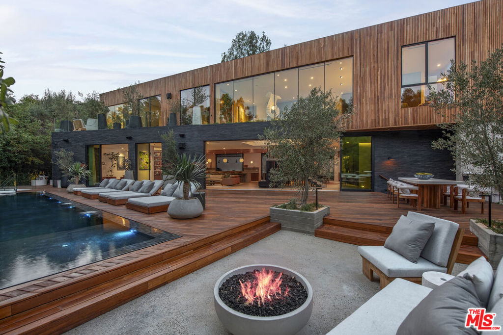 Welcome to a triumph of design and detail; a sanctuary of transitional Scandinavian modern design in the prestigious Beverly Hills neighborhood. This six-bed, nine and a half bath new construction home, with interior design by Abramson Architects, blends unparalleled craftsmanship with contemporary elegance and timeless sophistication. Nestled amidst majestic oak trees and serene canyon views, the estate invites you to immerse yourself in the ultimate luxury living experience.This architectural masterpiece is perched on a gated estate spanning almost an acre. Every detail has been thoughtfully curated, showcasing ultra-high-end materials, and organic bespoke finishes, resulting in a vacation-villa ambiance. The striking exterior, adorned with warm teak wood siding and black basalt stone, is both inviting and architecturally stunning, while mature hedges ensure maximum privacy.Inside, 10+ foot ceilings and expansive Fleetwood pocket doors create a seamless indoor-outdoor flow, flooding the main living spaces with natural light, and a sense of effortless grandeur. A chef's dream, the large professional kitchen features a striking 15-foot custom stone island, top-of-the-line Miele appliances, a charming breakfast nook, and a large automated pop-up window that transforms the space for effortless al fresco entertaining. Transitioning upstairs, the substantial primary suite impresses with a serene ambiance, complete with dual custom closets, a striking plastered floating fireplace, a secluded deck overlooking verdant canyon vistas, and a spa-like bathroom featuring a steam rain shower and a custom birchwood sauna. An expansive 50+ foot skylight floods the upper level with natural light, where four bedrooms extend to private outdoor decks, further enhancing the home's connection to nature. The piece de resistance is the floating staircase, complimented by a one-of-a-kind chandelier art piece that hangs; a true showpiece. The backyard is a seamless extension of the home's main living spaces, and are equally captivating with a zero-edge infinity pool and spa with swim-up bar, multiple fire pit lounges, pergolas, and fully equipped outdoor kitchensperfect for entertaining or peaceful relaxation. The lower level is a haven for recreation and entertainment, and is thoughtfully and artistically curated highlighting a pickleball court with stadium-like seating, pergola, grassy knoll with lush landscaping and hand-made fountains, all framed by the breathtaking beauty of the surrounding nature.Additional amenities include a secondary chef's kitchen, tiered private theatre, state-of-the-art home gym, office with custom cabinetry, temperature-controlled wine storage, showcase 3-car garage, parking up to 10 cars, two well-appointed laundry rooms, and Savant-powered smart home technology for modern convenience. The home is accompanied by custom-made indoor and outdoor furniture specifically deigned to fit within the Mid-Century Scandinavian design.The Hutton House is a private oasis of luxury and serenity where thoughtful design meets understated elegance. Every element reflects a commitment to quality and comfort, offering every conceivable amenity to those who demand nothing less than perfection. A rare opportunity to own a truly exceptional home in one of the world's most coveted locations.