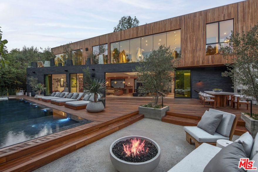 Welcome to a triumph of design and detail; a sanctuary of transitional Scandinavian modern design in the prestigious Beverly Hills neighborhood. This six-bed, nine and a half bath new construction home, with interior design by Abramson Architects, blends unparalleled craftsmanship with contemporary elegance and timeless sophistication. Nestled amidst majestic oak trees and serene canyon views, the estate invites you to immerse yourself in the ultimate luxury living experience.This architectural masterpiece is perched on a gated estate spanning almost an acre. Every detail has been thoughtfully curated, showcasing ultra-high-end materials, and organic bespoke finishes, resulting in a vacation-villa ambiance. The striking exterior, adorned with warm teak wood siding and black basalt stone, is both inviting and architecturally stunning, while mature hedges ensure maximum privacy.Inside, 10+ foot ceilings and expansive Fleetwood pocket doors create a seamless indoor-outdoor flow, flooding the main living spaces with natural light, and a sense of effortless grandeur. A chef's dream, the large professional kitchen features a striking 15-foot custom stone island, top-of-the-line Miele appliances, a charming breakfast nook, and a large automated pop-up window that transforms the space for effortless al fresco entertaining. Transitioning upstairs, the substantial primary suite impresses with a serene ambiance, complete with dual custom closets, a striking plastered floating fireplace, a secluded deck overlooking verdant canyon vistas, and a spa-like bathroom featuring a steam rain shower and a custom birchwood sauna. An expansive 50+ foot skylight floods the upper level with natural light, where four bedrooms extend to private outdoor decks, further enhancing the home's connection to nature. The piece de resistance is the floating staircase, complimented by a one-of-a-kind chandelier art piece that hangs; a true showpiece. The backyard is a seamless extension of the home's main living spaces, and are equally captivating with a zero-edge infinity pool and spa with swim-up bar, multiple fire pit lounges, pergolas, and fully equipped outdoor kitchensperfect for entertaining or peaceful relaxation. The lower level is a haven for recreation and entertainment, and is thoughtfully and artistically curated highlighting a pickleball court with stadium-like seating, pergola, grassy knoll with lush landscaping and hand-made fountains, all framed by the breathtaking beauty of the surrounding nature.Additional amenities include a secondary chef's kitchen, tiered private theatre, state-of-the-art home gym, office with custom cabinetry, temperature-controlled wine storage, showcase 3-car garage, parking up to 10 cars, two well-appointed laundry rooms, and Savant-powered smart home technology for modern convenience. The home is accompanied by custom-made indoor and outdoor furniture specifically deigned to fit within the Mid-Century Scandinavian design.The Hutton House is a private oasis of luxury and serenity where thoughtful design meets understated elegance. Every element reflects a commitment to quality and comfort, offering every conceivable amenity to those who demand nothing less than perfection. A rare opportunity to own a truly exceptional home in one of the world's most coveted locations.