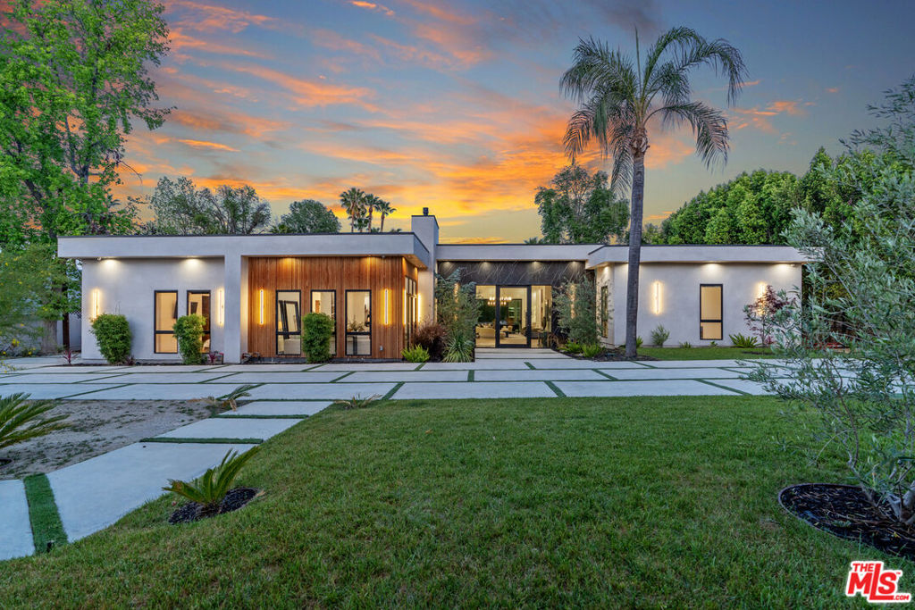 Experience the epitome of upscale LA living in this stunning single-story modern estate, offering nearly 7,000 sq ft of refined living space on a rare and private 0.6-acre lot. Soaring 14-foot ceilings and walls of glass define the home's expansive, open-concept layout, seamlessly blending indoor and outdoor living. Private and luxurious, this meticulously built home is a true masterpiece of scale, design, and craftsmanship. The heart of the home is an awe-inspiring great room that opens to a resort-style backyard, perfect for entertaining or serene everyday living. The chef's kitchen is a showstopper, featuring a jumbo island with seating, top-of-the-line appliances, and a built-in Miele coffee system. A large family room adds to the home's comfortable and luxurious flow. With 6 spacious bedrooms, each with en suite baths and generous closets, this home ensures privacy and comfort for loved ones and guests. The primary suite lives like a luxury boutique hotel room, complete with sitting area, fireplace, and sliding doors leading out to a private back patio. The spa-inspired primary bath includes a soaking tub, oversized walk-in shower, and expansive vanity space. For the ultimate cinematic experience, the property boasts a state-of-the-art home theater with soaring ceilings, ambient lighting, built-ins, a full bath, and a beverage center. Step outside to your private oasis, featuring a sparkling pool and spa with a Baja shelf, bubblers, fountains, and loungers. The fully equipped outdoor kitchen, ample covered seating, and cozy fire pit area make this a dream home for gatherings and entertainers. Additional features include dual gated driveways, a circular drive, a detached 3-car garage, a temperature-controlled office, and parking for up to 7 more vehicles in the motor court. Perfect for car enthusiasts and collectors. All built for today's discerning modern buyers needs including control 4 home automation system, motorized shades in bedrooms, large wine storage closet with beautiful glass display and custom lighting throughout. A rare offering of space, style, and seclusion in prime Tarzana, this one-of-a-kind property is not to be missed.