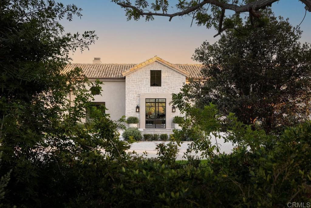 A masterful expression of timeless French country elegance, 17845 Via De Fortuna is meticulously rebuilt from the ground up to reflect the artistry and craftsmanship of a historic European manor. Set on 3.66 acres in the prestigious Rancho Santa Fe Covenant, this 10,363 sq. ft. masterpiece boasts 5 bedrooms, 5 full and 3 half baths, including a dedicated office and detached guest house. From the moment you arrive, the estate’s hand-selected antique barrel roof tiles from the South of France, signal an extraordinary level of detail. Antique oak beams, while hand-forged steel-framed windows and doors flood the home with natural light. The great room, anchored by a custom fireplace lined with reclaimed black firebrick, flows effortlessly into the exquisite Christopher Peacock kitchen, where La Cornue and Miele appliances, hand-painted cabinetry, and Afyon white marble countertops create a space that is as functional as it is breathtaking. The primary suite is a serene escape, offering a spa-inspired bath wrapped in Michelangelo marble, a deep soaking tub, and sweeping views of the lush gardens beyond. The outdoor spaces are a dream come true, where the estate’s natural beauty comes to life. A French village water basin turned fountain and the zero-edge pool and spa with the picturesque backdrop of the majestic Black Mountains create an unparalleled sense of tranquility. The outdoor kitchen, featuring a Kalamazoo grill, is perfect for al fresco dining under the stars, while a porch swing tucked behind the guest house invites moments of quiet reflection. The estate is offered fully furnished, with each piece thoughtfully curated to complement the home’s aesthetic. With state-of-the-art technology, including Lutron smart home automation, owned solar, Tesla backup batteries, and a comprehensive security system, this estate delivers unparalleled functionality alongside its exquisite design.