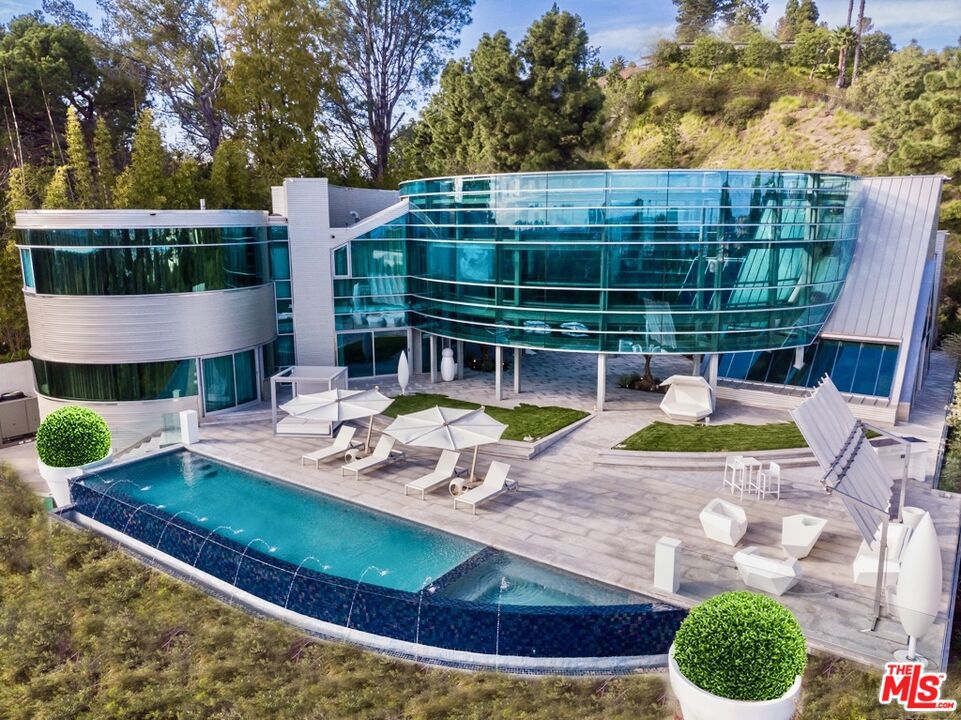 This estate is also being offered for sale. A sculptural glass and steel showpiece by renowned architect Edward R. Niles, this one-of-a-kind estate crowns a private knoll within the City of Beverly Hills, offering full city services and global prestige. Tucked at the end of a quiet cul-de-sac with unobstructed views from downtown to the ocean, the residence is defined by sweeping circular glass walls, a curving steel structure, and a dramatic central courtyard that seamlessly integrates indoor and outdoor living. Designed as a living sculpture, the home features six bedrooms, seven bathrooms, a private elevator, 7-car garage, infinity-edge pool, and light-filled interiors that capture panoramic vistas from every angle. Privately leased by high-profile individuals and featured in global media, this is a rare architectural iconnearly impossible to replicate under current Beverly Hills guidelines. The residence is currently offered for sale at $31,999,000 (MLS #25535879)