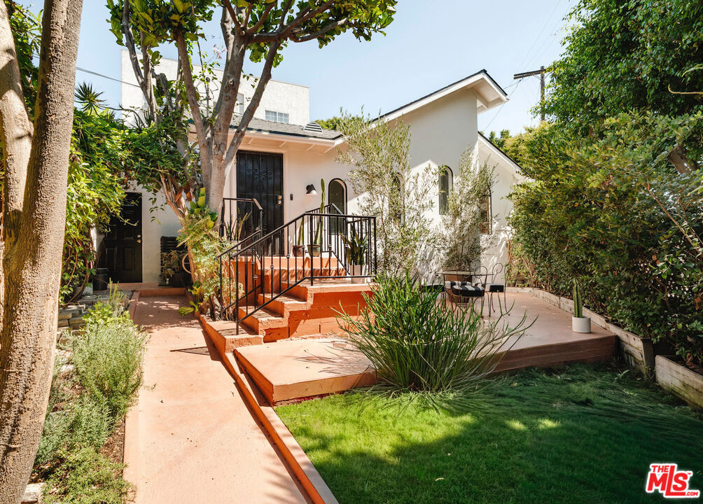 Set back from the street behind wood fencing and mature trees, this private 2 bed, 2 bath Silver Lake home offers 1,030 sq. ft. of elevated interior design, expertly curated outdoor space, and timeless architectural character. Ideally located, the cozy bungalow is a block from commercial offerings like Maury's Bagels and Psychic Wines, and a short distance from the Sunset Junction and Silver Lake Reservoir - a private retreat in LA's trendiest neighborhood. Past the front wooden gate, find the elegant yard, bordered by mature hedging and trees, with a grassy lawn and large patio ideal for home entertainment and outdoor dining. The front door opens to the open concept plan, with maple hardwood flooring extending throughout and light flooding in from arched front windows. The kitchen looks over the front living room, with a center peninsula allowing bar seating and conversation. Expertly appointed, the kitchen offers abundant cabinetry, quartz countertops, floating shelves, and plenty of room for cooking and hosting. Adjacent, the dining nook is anchored by a striking Entler chandelier, with sliding glass doors to the back that fill the main living space with sunlight. The gorgeous upstairs bedroom features a large front curved window with views of greenery, and is outfitted with a custom built-in bookshelf and desk, and a spacious closet. The dramatic ensuite bathroom features amber Zia zellige tile extending from the floor through the shower, and a refined slatted wood vanity with striking bulbous sconces. Stairs lead down to the primary bedroom, with a custom, pull-out closet and charming ensuite bathroom with a square tiled shower and bathtub. Additional features include a dedicated laundry and storage room, a gated side driveway, and a front courtyard perfect for alfresco dining. Comfortable and chic, the home is a rare offering in the heart of Silver Lake.