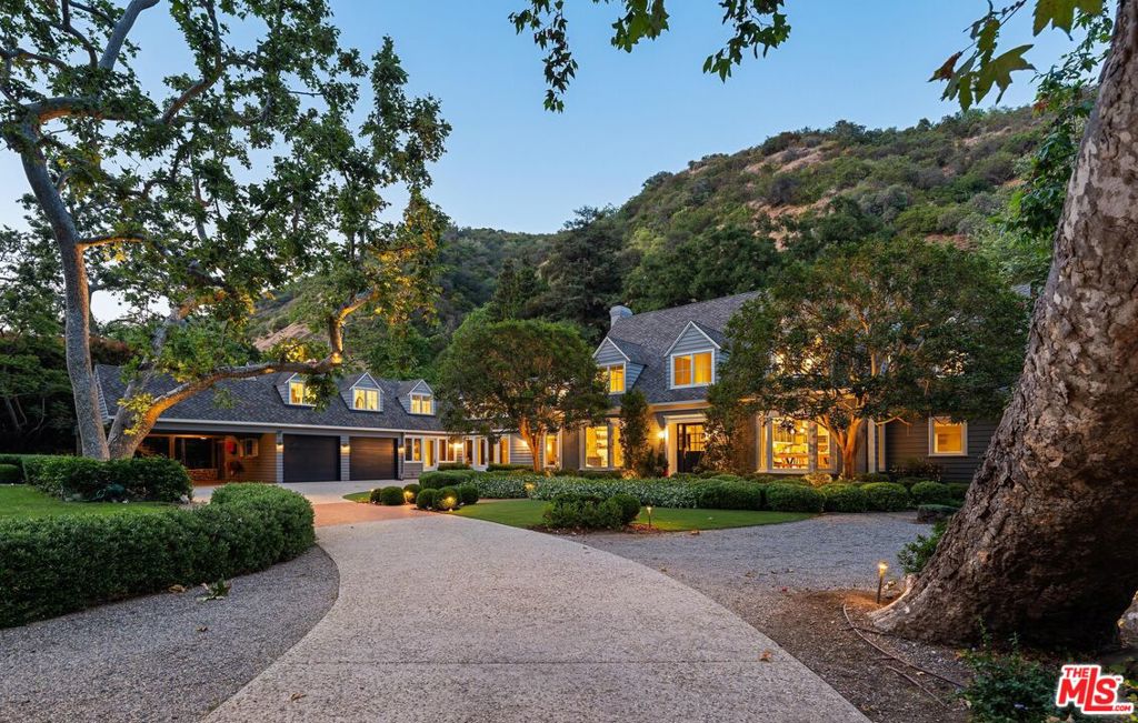 Nestled within the prestigious enclave of Mandeville Canyon, this exceptional gated estate offers an unparalleled 1.2-acre sanctuary beneath a majestic canopy of mature sycamores and oaks. Reimagined with precision and timeless vision, the 8,476-square-foot Hamptons-style residence is a masterclass in quiet luxury, blending heritage charm with contemporary sophistication to create a haven for both elegant entertaining and relaxed everyday living. Comprising eight bedrooms and ten baths, the estate has been thoughtfully curated to exude a refined sensibility. Inside, a luminous interior unfolds with reclaimed wood beams, rich oak hardwood floors, and expansive glass doors that dissolve the boundary between indoors and out, imbuing the home with warmth, texture, and a seamless connection to nature. The heart of the home is a chef's kitchen of rare caliber designed for the culinary aficionado with a 60" Wolf range, triple SubZero refrigeration, dual dishwashers, three sinks, and a generous walk-in pantry. Adjacent informal dining and a cozy TV alcove offer spaces for intimate gathering, while the formal living and dining rooms provide an ideal backdrop for sophisticated soirees. Anchoring the estate is a breathtaking two-story great room, perfectly appointed for entertaining, complete with a full bar, temperature-controlled wine cellar, and bespoke entertainment center. A richly paneled private study with a full bath offers a serene workspace or stately library retreat. Beyond the main residence, a detached one-bedroom guest house with private entrance and secluded patio offers guests a luxurious, autonomous escape. Two en-suite staff or flex bedrooms provide versatility for a home gym, office, or additional accommodations. Upstairs, the primary suite is a sanctuary of serenity, capturing treetop vistas and thoughtfully designed with a beverage bar, a marble-clad spa bath featuring a freestanding soaking tub and indulgent steam shower, and an expansive custom walk-in closet. Each additional bedroom suite offers its own tranquil ambiance, adorned with classic detailing and bathed in natural light. Outside, the grounds evoke a resort-like sensibility: a stunning ozone-purified pool and spa invite restful retreat, while fire tables, heated lounges, and a fully equipped outdoor kitchen create the ultimate stage for al fresco entertaining. A lighted pickle ball court encourages active recreation, while a treehouse and playground provide whimsical charm for all ages. Privately hedged and gated, with motor court parking for over 12 vehicles, including a two-car garage and a two-car carport the property is secured by a cutting-edge security system and offers the rare blend of seclusion and accessibility.Ideally located moments from the Brentwood Country Mart, world-class dining, luxury shopping, and scenic hiking trails, this remarkable estate is not merely a residence, it is a lifestyle defined by grace, privacy, and enduring sophistication.