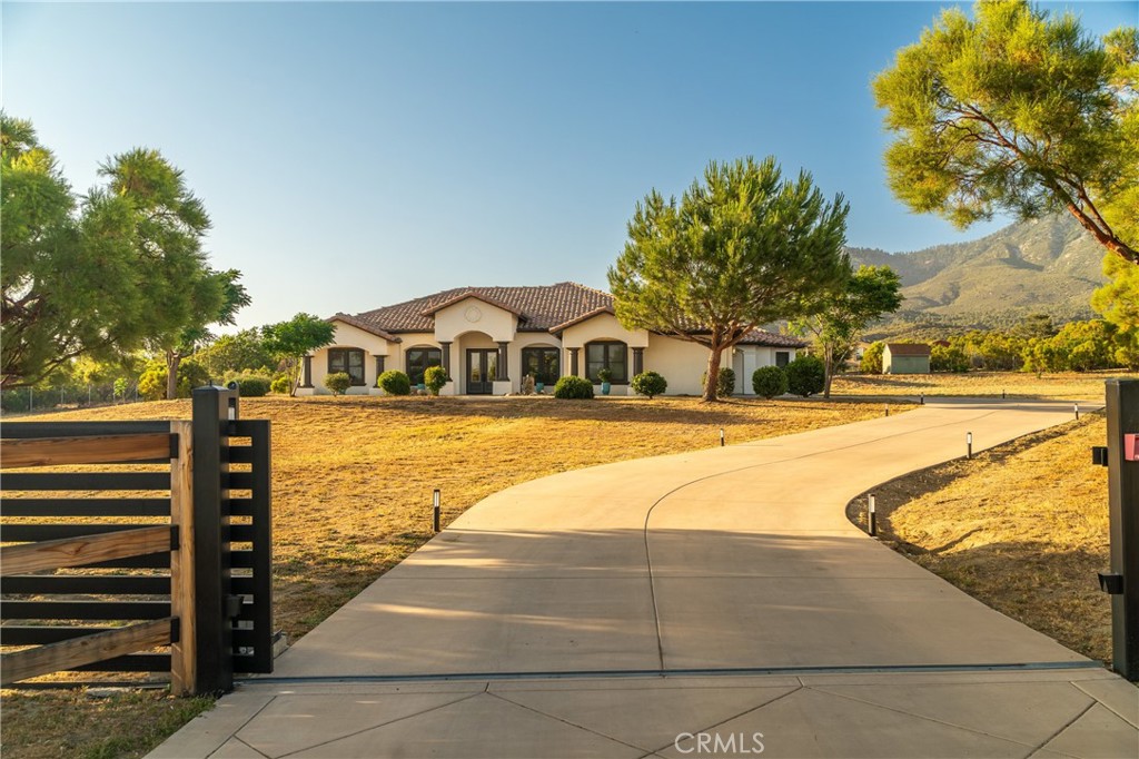 Step into this stunning, turn-key, custom-built 4-bedroom, 3-bathroom home, where no detail has been overlooked. Located in a prime spot with paved road access, this energy-efficient, super-insulated residence welcomes you with a custom automatic gate and a gracefully curving driveway, leading to a charming stone fountain at the entrance. Inside, discover a spacious, open-concept living area defined by tall, coffered ceilings and enhanced by custom doors, windows, architectural accents, and artful niches. The chef's kitchen is the heart of the home, featuring beautiful granite countertops, a built-in oven with microwave, a wine chiller, and a full-length eating bar perfect for family gatherings and entertaining. Enjoy your morning coffee in the breakfast nook with breathtaking mountain views from the bay windows that overlook the rear patio. The adjacent great room offers a cozy fireplace and a wall-mounted 85"OLED TV, with sliding glass doors opening to a covered patio for extended entertaining. A convenient walk-in pantry and half bath are just off the kitchen. The luxurious primary suite boasts a second fireplace, ample closet space, and private sliding glass door access to the covered patio. Indulge in the travertine-tiled bathroom, complete with a heated soaking tub. On the opposite side of the home, two bedrooms share a well-appointed bathroom with individual vanity areas. A fourth bedroom, currently used as an office, is conveniently located off the entry. The large laundry room includes a washer, dryer, space for a secondary refrigerator/freezer and ample cabinetry. The attached 3-car garage features two EV chargers and a whole-house water filtration system. Outside, the fully fenced and usable land has ample space for horses, orchards, gardens, and also features a full RV hookup with 50 amp power, storage buildings, ample lighting, and a relaxing jacuzzi tub on the back patio. This home truly offers a perfect blend of luxury, comfort, and thoughtful design. Seller is including a duel-fuel 12kw-back up generator. *** Be sure to check out the virtual tour which has additional information.