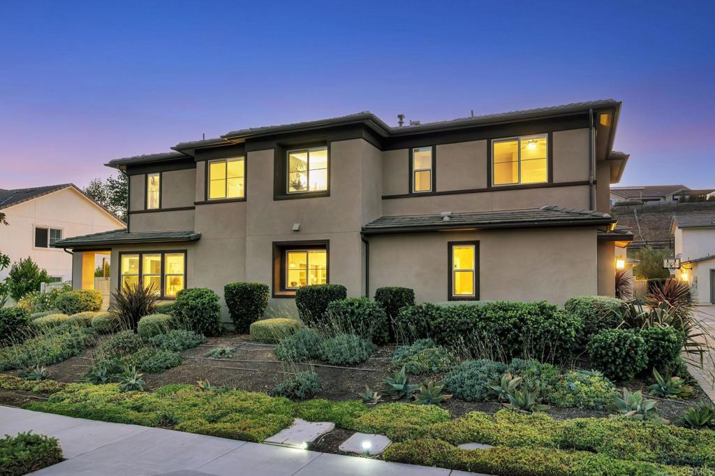 Beautiful two-story home in the sought-after Harmony Grove Village with extensive upgrades and smart-home features throughout. This Cavalli neighborhood home offers 2,928 square feet of living space, 4 bedrooms, 3 bathrooms, loft, a California Room with built-in fireplace, first level bedroom and full bathroom, solar panels, Ring doorbell, ADT security system, zoned HVAC, tankless water heater, smart LiftMaster garage opener & overhead storage racks, and a fully landscaped backyard with artificial turf, fruit trees, planter boxes, and pre-engineered utilities for gas, plumbing, and electric. The open-concept main floor is enhanced by recessed lighting, designer fixtures, and a custom wood accent wall at the entry. The spacious living area includes a striking black accent wall, sleek ceiling fan, and large windows that flood the room with natural light. Sliding doors lead to the covered California Room that includes a fireplace w/ Monterrey Black slate surround, pre wired recessed TV space, and Nepal Gray porcelain tile flooring—perfect for year-round indoor-outdoor living. The gourmet kitchen features a large quartz island with seating and pendant lighting. Rich dark green paint on the island base and lower cabinets contrasts beautifully with the white upper cabinets and full tile backsplash. Golden brass hardware, under-cabinet lighting, stainless steel smart appliances, a deep dual-basin sink, and a built-in retractable trash/recycling system combine style with convenience. A coffee station with matching backsplash sits next to a spacious walk-in pantry with built-in shelving for excellent storage. Downstairs includes a guest bedroom with walk-in closet and a beautifully updated bathroom featuring a glass-enclosed walk-in shower with seating bench. Upstairs, a bright and versatile loft with vertical wood slat accent wall, custom limewash finish on another wall, and recessed lighting provides the perfect space for a media room, play area, or office. Two additional bedrooms feature large windows and white wood closet doors—one showcases a custom jungle-themed accent wall, while the other includes a ceiling fan for added comfort. A hallway cabinetry station adds extra storage. The luxurious primary suite features recessed lighting, sliding glass doors to an oversized private balcony, and direct access to an expansive walk-in closet with built-ins and double mirrored doors. The spa-inspired primary bathroom offers separated dual-sink quartz vanities, large soaking tub with tile accents, separate glass-enclosed shower, oversized mirror, recessed lighting, and neutral tile flooring for a clean, contemporary look. The upstairs laundry room is equipped with GE washer and dryer, sink, extended counter space, and abundant upper and lower cabinets for organization. Outdoor living is maximized with a fully fenced backyard featuring artificial turf, string lights, planter boxes, fruit trees (lemon, orange, persimmon, papaya, eggplant, mint), cement patio area, tool shed, and side yard with concrete steps and space for garbage cans. Additional highlights include smart Caseta Wireless LED dimmers, Google Nest thermostat, Alexa Echo Show, Blink outdoor cameras, and a robust Ruckus mesh Wi-Fi system ensuring seamless coverage throughout the home. The garage features smart tankless water heater and water softener controls plus extensive overhead storage. Harmony Grove Village is a master planned community with gorgeous mountain ridgeline views, multipurpose trails, gated pool for homeowners, dog and equestrian park, multiple private parks and the huge 4th of July Park (open to the public). The Grove is the perfect place to enjoy the outdoors- it includes the pool, jacuzzi, wading pool, barbeques, shaded tables, play structure and a covered lounge area with outdoor furniture and fireplace.