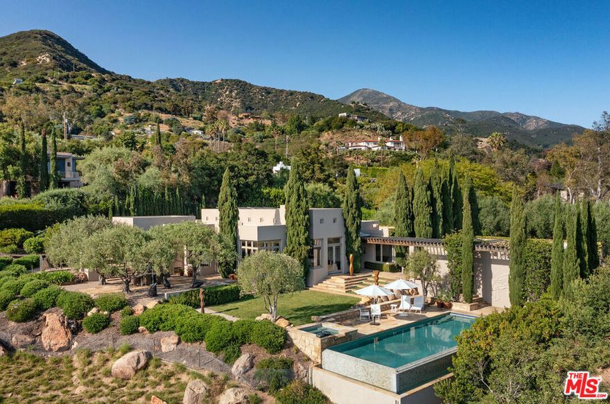 A sophisticated retreat in the hills of Montecito, this architectural gemdesigned by internationally renowned Barry Berkusboasts incomparable views of the harbor, Pacific Ocean, Channel Islands, and beyond. The 4-bedroom, 4-bath residence is a masterful expression of bold lines, soaring ceilings, and light-filled interiors. Champagne limestone floors flow continuously throughout the home. The landscaping, curated by acclaimed designer Mark Rios, elevates the outdoor experience with serene gardens featuring a koi pond, lavender beds, an infinity-edge pool with spa, towering cypress trees, climbing bougainvillea, and a charming alfresco dining area shaded by century-old olive trees. This is a Mediterranean daydream-just ten minutes from Coast Village Road and Butterfly Beach.A beautifully carved door marks the entry, revealing an alle of cypress trees that sets the tone for the tranquil elegance within. The open-plan living and den areas feature 15-foot ceilings, exposed wood beams, a skylight, and clerestory windows that bathe the space in natural light. Defined without walls, the layout flows effortlessly. Just off the main living area, a spacious private study-or optional fourth bedroom-offers flexibility and privacy. The kitchen and dining areas, accessed through another set of French doors, are designed for both function and beauty. Oversized windows frame panoramic views, while a central Caesarstone island anchors the space. Top-of-the-line appliances include a Viking cooktop and ovens, Sub-Zero refrigeration, and Miele appliances. A few steps above the main level, the bedroom wing includes two en-suite guest rooms and a beautifully reimagined primary suite. The primary suite enjoys its own private patio with ocean views, a luxurious dressing area with custom European-style closets, and a serene spa-like bath. Picture windows frame Japanese maples, while a soaking tub, seashell limestone counters, and bespoke cabinetry complete the sanctuary. Additional amenities include a Sonos sound system throughout the interior and exterior, newly installed solar panels with backup battery, and access to a shared private well with two neighboring residences. Located on a quiet private lane, this exceptional home offers the perfect balance of refined design and peaceful seclusion.