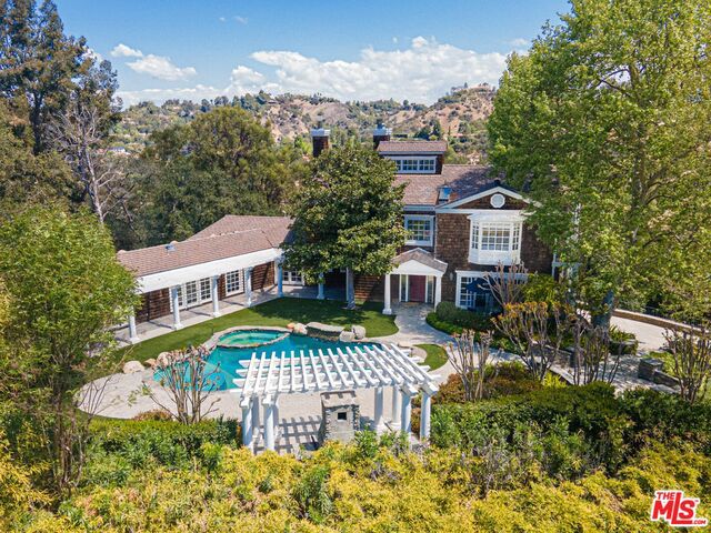 A dream opportunity to either develop or redesign on a stunning, oak-studded acre on an exclusive, gated street in Beverly Hills. Entering the gates, a long private driveway leads to an elegant Hamptons-style country estate that sits on vast, magnificent gardens and lawns perfect for entertaining on any scale. An artfully crafted, 3-level retreat with the finest organic materials that fully harmonizes with its natural surroundings. Open, spacious living spaces with double height ceilings and exquisite fireplaces invigorate the senses with their sheer volumes and rich natural light. Gourmet kitchen, formal living, dining & family rooms with floor-to-ceiling doors open to multiple outdoor entertaining areas: Massive 2-level wraparound decks, an oversized lawn and garden with a glistening pool/spa and a pergola lounge with a stone wood fireplace, in the serenity of mature, picture-postcard landscaping. 4 guest rooms including two with separate access and a standalone artist studio for additional accommodations. A charming, wooden bonus space with vaulted ceiling can be used as a gym or media room. Spacious primary suite features an exquisite bathroom with a soothing tub overlooking the pool. Live among the titans and elite in this coveted estate with infinite possibilities.