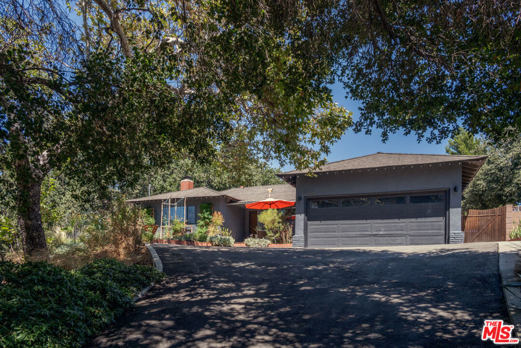 Tucked above the street and nestled beneath a canopy of mature oaks, this timeless Mid-Century home looks out over Happy Valley. Lush garden beds invite you into an open-concept space, where living and dining areas are bathed in natural light throughout the day, anchored by a classic stone fireplace. Sliding doors flow seamlessly to the backyard - ideal for al fresco dining, entertaining, or peaceful mornings in the garden amidst the fruit trees. A large, renovated kitchen is equipped with a premium Bosch oven & stove and adjoins a dedicated laundry room and an oversized two-car garage, offering ample storage. Down the hall, an ensuite primary bedroom opens to the yard through sliding doors. Two additional bedrooms share a full bath, making the layout both functional and spacious. Recent upgrades include a 200-amp electrical panel, new dual-pane windows, new wood flooring, and a greenhouse. Situated on an expansive 11,000+ sq ft lot, the property features a level, lower pad - offering potential for a future ADU, studio, or home office (buyer to verify). The natural topography and elevated positioning provide exceptional privacy, rare for such a central location. Just moments from Old Town, Main Street, the farmer's market and the train station - and close to Magic Mountain and Cal Arts. A unique opportunity to own a thoughtfully preserved and upgraded Mid-Century gem in one of Newhall's most beloved neighborhoods.