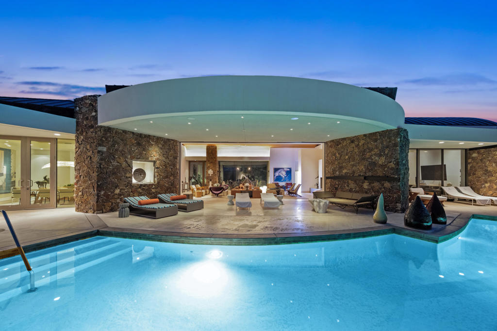 Discover timeless sophistication in this iconic modernist masterpiece by acclaimed architect Narenda Patel recently remodeled. Situated within the exclusive guard-gated Waterford community of Mirage, this 7,374-sq-ft estate offers 5 bedrooms and 8 baths of unparalleled craftsmanship and luxury. Arrive through a sculptural entryway to interiors clad in Portuguese white limestone, wide-plank white oak, and plush Berber carpet. Dramatic 9′ to 18′ ceilings and 9′ solid-core doors frame a seamless indoor-outdoor flow, enhanced by automated shades and ambient lighting. The completely reimagined chef's kitchen boasts bespoke cabinetry, top-tier appliances, and an adjoining butler's pantry. Entertain effortlessly in the great room or alfresco under the desert sky. Retreat to the grand primary suite, featuring dual spa-like baths, two walk-in closets, and a private lounge with floor-to-ceiling views. Four additional en-suite bedrooms ensure comfort and privacy for family and guests. Sustainably powered by a fully owned 100-panel solar system and equipped with an EV charging station, advanced Control4 home automation handles audio/visual, security, and climate control at your fingertips. Outside, reimagined landscaping and integrated lighting create a serene oasis, complete with multiple seating areas and pristine hardscaping. A rare offering in one of Rancho Mirage's most coveted enclaves--experience modern desert luxury at its finest.