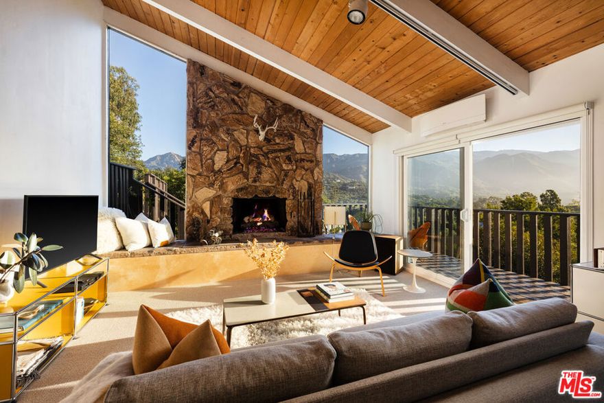 This Riviera Summit mid-century retreat, set on approximately one acre, embodies a rare harmony of architecture and nature. Just minutes from downtown Santa Barbara and Montecito's shopping and dining, the serene multi-level residence is celebrated for its architectural significance, mountain vistas, sunrises and moonrises, and daily encounters with deer, hawks, and the evening song of coyotes. The home's open layout blends European sensibility with Santa Barbara's signature indoor-outdoor living, seamlessly connecting the main living, kitchen, and dining spacesappointed with high-end appliancesto multiple view decks, ideal for year-round entertaining, al fresco dining, and relaxed lounging. Arrival is marked by a distinctive entry deck designed around two graceful oak trees, leading to a calming water fountain. Inside, expansive windows, beamed ceilings, and a striking stone fireplace frame mountain views that serve as living artwork. The private primary suite occupies its own level, offering a sitting area, fireplace, generous closet, flexible office space, and a secluded deck that heightens the sense of retreat. Its spa-like bath features a soaking tub with views to the natural surroundings. Freshly painted inside and out, with a new roof and gutters, the residence offers peace of mind along with timeless style. Bordered by Franceschi and Parma Parks, the home is immersed in nature with world-class hiking and cycling just outside the door. Below the residence, the gently sloping acre invites possibilities: a pool, orchard, enhanced landscaping, or an ADU with existing design plans and site approvals, an opportunity to expand this mid-century gem into a multi-generational enclave or guest retreat.