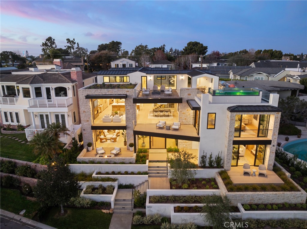 Poised on an elevated lot on prestigious Kings Road in Newport Beach this newly constructed organic contemporary home offers a panorama of impressive ocean and harbor views and blends modern design with natural elements to create a serene and inviting living environment. Conceptualized by architect Eric Aust and constructed by Gonterman Custom Homes the residence spans over 6400sft on three levels and features six bedrooms, six full and three half baths, theater, gym, library, elevator, and rooftop pool. Incorporating a sophisticated blend of natural wood and stone materials, complemented by bespoke fixtures and lighting, the home’s expansive layout lends itself to both comfortable everyday family living and impeccable grand-scale entertaining. Surrounding a meditative courtyard garden and covered lounge area with fireplace, the entry level presents two distinctive bedroom suites, theater, and handsome library/den that opens to terrace. Ascend a striking glass and wood staircase and be greeted by an impressive great room that conveys style and refinement. Here the open-concept space merges the luxurious living area, professional grade kitchen with service kitchen and dining room with wine wall, all designed to frame water views. Retreat to the primary suite designed for rest and rejuvenation. The adjoining spa-inspired ensuite is a haven of relaxation and features soaking tub, oversized walk-in shower, dual vanities and premium fixtures. A custom-designed walk-in wardrobe adjoins. Two generously proportioned guest suites are thoughtfully designed with high ceilings, large windows and luxurious ensuites. Seamlessly integrating indoor and outdoor living, the home’s third level is where style, comfort and function converge. Step into the exercise room that enjoys abundant water views. An adjoining guest suite with sitting area opens to its own patio. Truly an elevated experience, the rooftop terrace is designed for indulgence and relaxation and the abundant water views serve as a reminder of the home’s exceptional setting. An entertaining oasis the retreat features a professional-grade outdoor kitchen replete with pizza oven, a jetted pool/spa, and a fire pit sitting area that invites guest to linger and revel in the panorama of water and city light views. Equipped with home automation and security, five fireplaces, elevator servicing all levels, three car garage, mud room, laundry room, and study retreat, this exquisitely crafted home exceeds expectations.