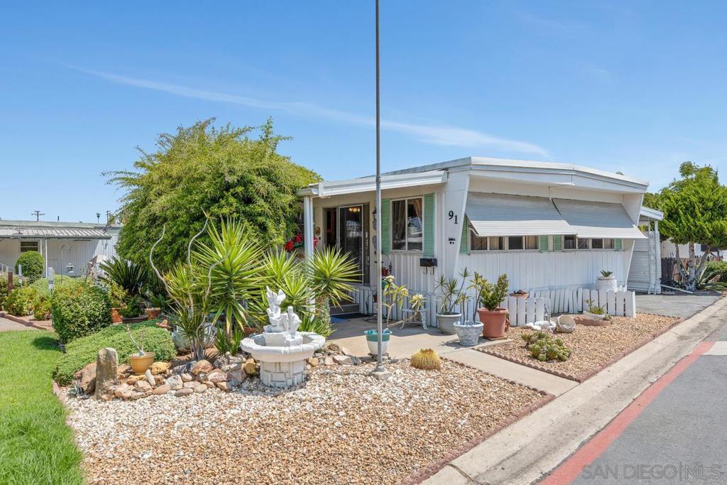 Welcome to this 55+ park in El Cajon. Space #91 is located on a corner lot with guest parking right in front. A green lawn and trees frame the home for shade and privacy. Cool breezes await you on the covered porch. Inside you will find a spacious primary bedroom with ensuite bath, a large living room w/ many windows, a full kitchen, laundry hookups- washer hookups inside, gas dryer hookups in shed in carport. This quiet neighborhood offers many activities w/ a pool, spa, Wednesday potlucks, Bingo, and a community center w/ games and puzzles. (Refrigerator, washer/dryer do NOT convey.) There is a smaller 2nd bedroom and a hall bath with shower. Home needs some love and is priced for condition. Space rent is $1395 +utilities. Please get approved before putting in offer.