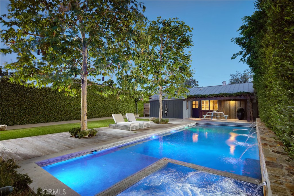 Serene, private and casually luxurious, this genuinely rare home in Newport Beach’s preferred Bayview Heights equestrian neighborhood presents the ultimate expression of Modern Farmhouse style. Settled on an all-flat site of .41 acres, the expansive single-story design reveals approximately 3,612 square feet of custom living space that retains the warmth of its humble beginnings while showcasing a host of bespoke refinements and thoughtful expansions. Charming curb appeal is elevated with a windmill, custom fountain, elevated planter beds, and a long custom driveway that extends almost the entire depth of the property and generously accommodates guest parking. An inviting Dutch door opens to the entry, which leads to the living areas and a separate bedroom wing. Primed for outstanding entertaining, the great room and kitchen area is crowned by a vaulted open-beam 20' ceiling and displays a floor-to-ceiling fireplace with raised hearth, and three sets of French doors leading to the backyard. A 13' island anchors the chef's kitchen, where a stone wall harmonizes with custom Shaker cabinetry, open shelving, Carrara marble countertops, and a large walk-in pantry with built-in desk. Top-of-the-line appliances include a BlueStar French-door oven, Thermador cooktop, cabinet-matched Sub-Zero freezer, and a professional-grade Traulsen refrigerator with access from the kitchen and pantry. Four bedrooms and four baths include a fireplace-warmed primary suite with lux bath. Beyond a reimagined backyard with newer pool and spa awaits a magnificent barn with poolside patio, walk-in wet bar, partial kitchen, lounge/game area, chicken coop, and an after-swim shower. Designed by architect Eric Olsen, this light and welcoming residence is detailed with reclaimed wood floors, reclaimed bathroom sinks, skylights, custom lighting and window treatments, owned solar, whole-home water filtration system, and state-of-the-art smart-home tech from Lutron, Sonos and Control4.