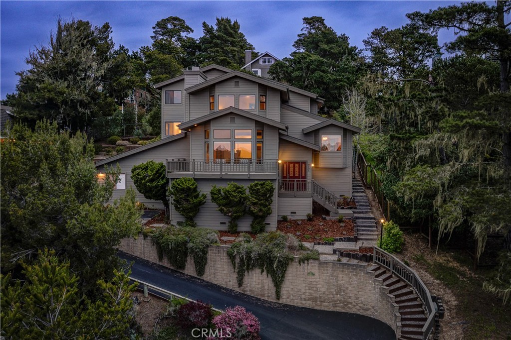 Perched gracefully on a 0.23-acre lot amidst Cambria’s iconic Monterey Pines, “Vista del Pino” is a tri-level sanctuary capturing the essence of timeless coastal elegance. Gaze out across sweeping ocean vistas and tranquil pines from every room. This meticulously crafted three-bedroom, three-bathroom residence—an expression of architectural harmony—features soaring wooden plank ceilings, a fully enclosed sunroom, and skylights throughout. Step onto the wrap-around balcony and be enveloped by 360-degree views—a perfect setting for morning reflections or golden hour reveries.
Ascend to the upper level, where the primary suite—with panoramic views—merges with the soothing comforts of an oversized ensuite bath, complete with a jetted soaking tub. Outdoors, a tiered garden invites creativity and connection with the land—an idyllic canvas for green thumbs. A private drive leads to a freshly painted two-car garage, adjacent parking, and a versatile basement flex space. “Vista del Pino” offers a rare opportunity to live in a serene retreat that harmonizes with the land, the sea, and the enduring spirit of Cambria.