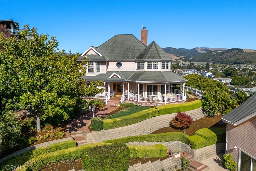 Perched above the historic Village of Arroyo Grande, this timeless Victorian farmhouse offers sweeping views of the city, surrounding mountains, and the Pacific Ocean—along with a DETACHED STUDIO and a spacious bonus room above the garage, ideal for a shop or creative work. Inspired by San Francisco’s iconic Painted Ladies, the home was thoughtfully crafted to be historically accurate and built to last a century.
Set on nearly half an acre, the home greets you with a wraparound veranda and an elegant octagonal cupola—signature details from the Victorian era. Inside, a soaring two-story foyer showcases a grand staircase, antique chandeliers, and Casabella plaster rosettes. French doors open to an octagonal living room featuring coffered ceilings, custom built-ins, and a fireplace with wood mantel and sconce lighting.
The living room connects to the formal dining room via a double-sided fireplace. From here, two sets of French doors lead to the veranda and backyard—perfect for seamless indoor-outdoor entertaining. The kitchen features a generous L-shaped island, Sub-Zero refrigerator, and double ovens, and opens to a warm family room with coffered ceilings and fireplace.
Just off the kitchen, a charming cottage sunroom overlooks the Village and leads to the backyard, complete with gazebo, putting green, and a white picket fence that frames the entertaining space. A den on the main level adds flexibility for guests, a home office, or media room.
Upstairs, the octagonal primary suite offers dramatic views, coffered ceilings, a two-way fireplace, and a spa-like ensuite bath. Two additional bedrooms and a full bathroom complete the upper level.
The detached two-car garage houses a private studio and a large finished bonus room above—ideal for multigenerational living, a private office, or future expansion.
This is more than a home—it’s a Central Coast legacy property that honors the past while offering space, beauty, and flexibility for the future.