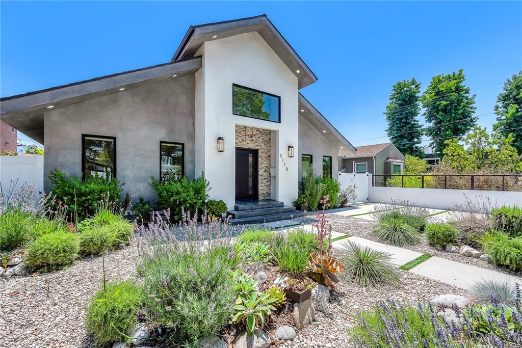Welcome to this stylish and thoughtfully designed modern French farmhouse in the heart of Sherman Oaks. From the moment you arrive, the bold front entry—featuring a contemporary chandelier and stone accent wall—sets the tone for what’s inside. Step into a bright, open two-story layout filled with natural light, wire-brushed Sahara oak floors, and custom designer touches throughout. The living and dining areas flow together seamlessly, highlighted by a striking stone wine wall and built-in ceiling speakers, perfect for entertaining. The chef’s kitchen is equipped with custom cabinetry, quartz countertops, and a premium Thermador appliance package. The adjacent family room features a large fireplace with elegant stonework and custom built-ins on both sides. Glass sliders open to a private backyard retreat with a built-in BBQ, sparkling pool and spa, and a fully equipped 2-bedroom, 1-bath guest house with its own kitchen, laundry, and separate address (5108 Greenbush Ave). Ideal for extended family, a guest suite, or rental income. Upstairs, the junior suite includes a full bathroom and Juliet balcony overlooking the pool. The spacious primary suite offers its own Juliet balcony and a spa-like bath with soaking tub, oversized rain shower, and skylight. Two additional junior suites are located on the main level, each with their own en-suite bathrooms. Smart features include built-in ceiling speakers (including patio), Ring doorbell, Ecobee smart thermostat, pre-wired WiFi/TV in every room, and a full alarm system. A gated front entry and elegant powder room add convenience and privacy. Lush, Low-Maintenance Garden Raised planter boxes with automatic irrigation overflow with tomatoes, herbs, and vegetables, while drought-resistant landscaping features charming South-of-France-style rocailles. Milkweed and flowering shrubs attract monarchs and hummingbirds, and a prolific lime tree and mature lemon tree provide fresh citrus year-round.