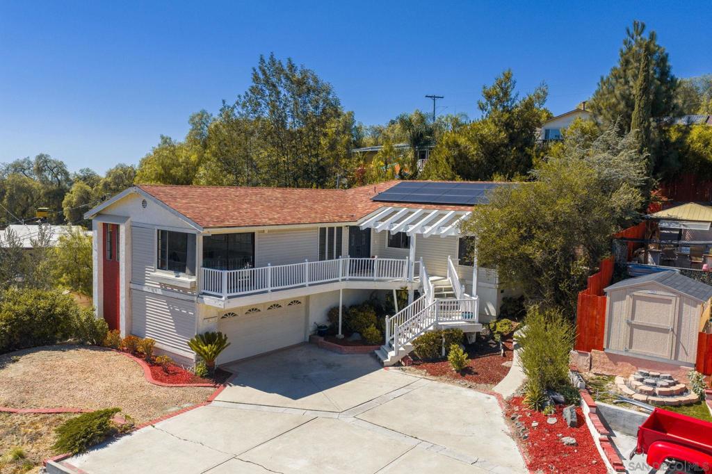 Stunning View Home in the Foothills of Casa de Oro & Mt. Helix. Perched high above Madrid Way with total privacy, this spacious home offers over 2,100 sq. ft. of living space, an attached 2-car garage, and ample parking. The flexible layout is ideal for multi-generational living, featuring a full bedroom and bathroom on the lower level with direct garage access. Upstairs, nearly every room enjoys sweeping views of the surrounding hills. The bright kitchen showcases crisp white cabinetry and counters, while the living room offers a cozy fireplace and picture-perfect views. The primary suite opens directly to the back patio for easy indoor-outdoor living. The backyard is designed for entertaining, complete with a detached game room, a covered patio for dining under the trees, and a firepit area for gathering with friends and family.