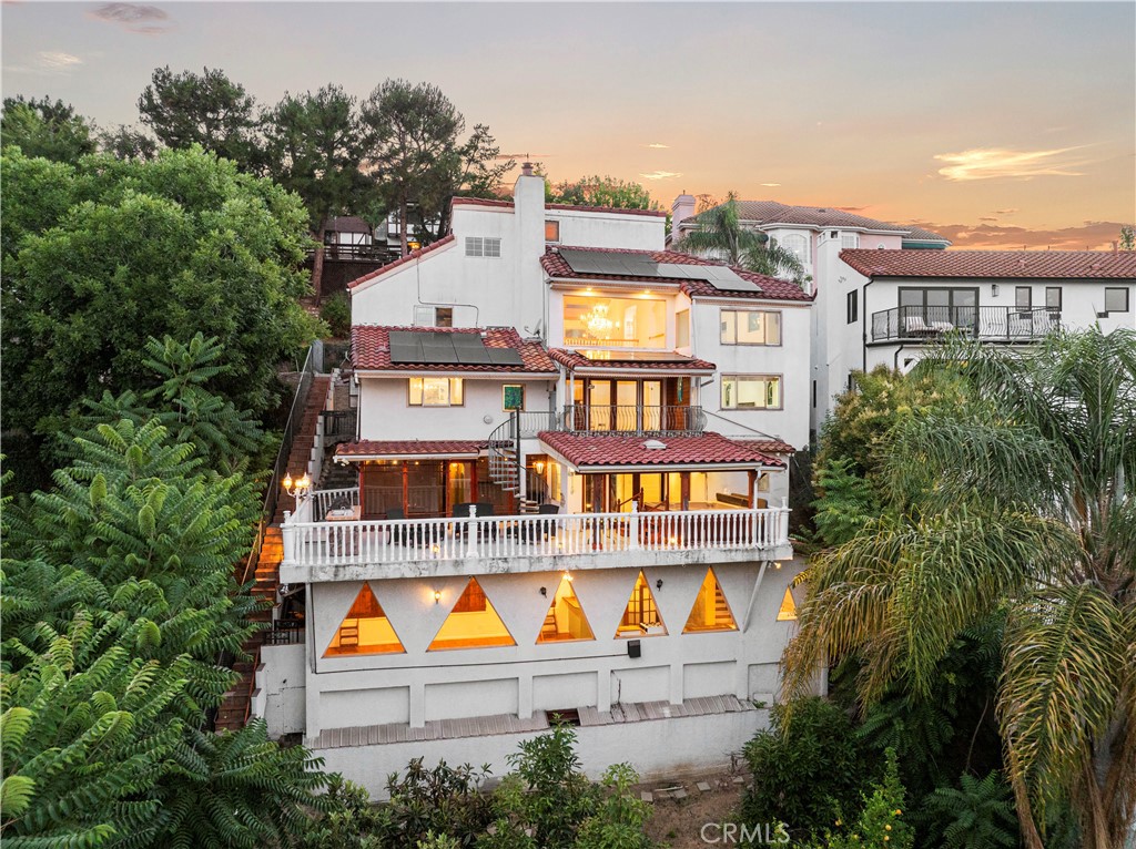 With incredible views and a commanding presence in the desirable Los Feliz Hills, this gated five level residence offers more than 3,200 square feet of living space with five bedrooms, four bathrooms, and a unique architectural layout designed for privacy, flexibility, and elevated living. Beyond the automatic gate and low maintenance front yard with artificial grass, you are welcomed by a dramatic entry featuring expansive windows, a statement chandelier, and a striking spiral staircase leading to the top floor, a bright open space ideal for a home office, yoga studio, or creative retreat. The entry level includes a spacious bedroom, a full bathroom, a laundry area, and direct access to the two car garage. One level down, the main living space offers high ceilings, tile flooring throughout, and an open concept kitchen, dining, and living room. The kitchen is equipped with granite countertops, a tile backsplash, quality appliances, custom cabinetry, and a large center island. This level also features the primary suite, complete with a large walk in closet and a spa inspired bathroom with an oversized walk in shower. A private staircase from the primary suite provides direct access to the second and first floors. The second floor below the main level includes two additional bedrooms, a full bathroom, an enclosed workout room, and a 450 bottle wine cellar. This level also opens to a large outdoor deck with built in BBQ, spa, and lounge seating area, perfect for entertaining while enjoying the peaceful hillside setting. The lowest level lives like an attached ADU with its own entrance, bar, and expansive living area framed by dramatic triangle windows. The ADU bathroom features a massive walk in shower, adding to its functionality and appeal for guests, extended family, or studio use. Exterior stairs connect the driveway to a private lower terrace highlighted by an eye catching decorative wall, ideal for outdoor dining, entertaining, or future customization. Owned solar adds energy efficiency and helps reduce utility costs. This one of a kind property offers impressive scale, versatility, and privacy in a premier Los Feliz location just minutes from the Greek Theatre, Griffith Park, Los Feliz Village, and the shops and restaurants along Hillhurst and Vermont.