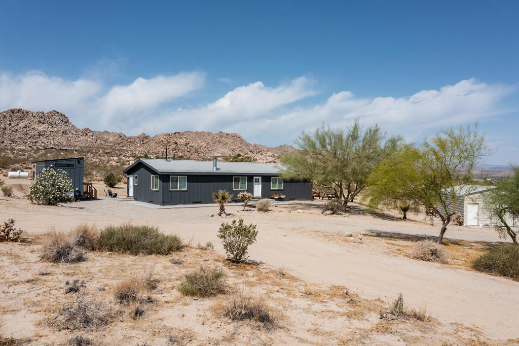 Designer remodeled home with skyline views! Set on 5+ acres of hillside in the highly desirable Panorama Heights neighborhood. Turn-key 2 bed 2 bath plus a large den that could be used as a 3rd bedroom with over 1,500sf. Pebble stone driveway with ample parking leads to the wraparound concrete patio and walkway to the front door. Living room with new floors, high sloped ceiling, recessed lighting, and gallery wall. Kitchen with new appliances, two breakfast bars with one as an island countertop. Stainless steel refrigerator, microwave, oven and cooktop, Abundant space with new cupboards and long counter tops. Additional dining area with built in cabinetry and glass sliders to the rear patio. Laundry room with double stack washer and dryer and butcher block counter. Large master bedroom with walk-in closet. Master bathroom with marble and glass shower. Guest bedroom with private bath. Backyard concrete patio enjoys picnic tables to enjoy dining alfresco with friends under the stars. STR permit approved. Inspiring views of the boulder studded mountains in the Joshua Tree National Monument. Captivating vistas for miles. Copper Mtn, Bunker Mtn, Mt Bartlette, the Bullion Mtns, and Mt San Gorgonio with snow capped peaks. Beautiful sunsets and shimmering city lights at night. Horse property. Less than 1000ft to the JTNM trails with gorgeous boulder gardens and canyons. Modern architectural new homes can be seen throughout the neighborhood. The high land value in Panorama Heights makes for sound investing. The county may allow for building another home and guest homes on this lot to expand your luxury compound. Short trip to organic restaurants, cafes, bars and boutiques in the JT Village. Close to the JTNM main gate where about 3 million tourists visit the park annually. 55 minutes to Palm Springs. Call for a showing today. (Tiny home on wheels & furniture is not included in the sale)